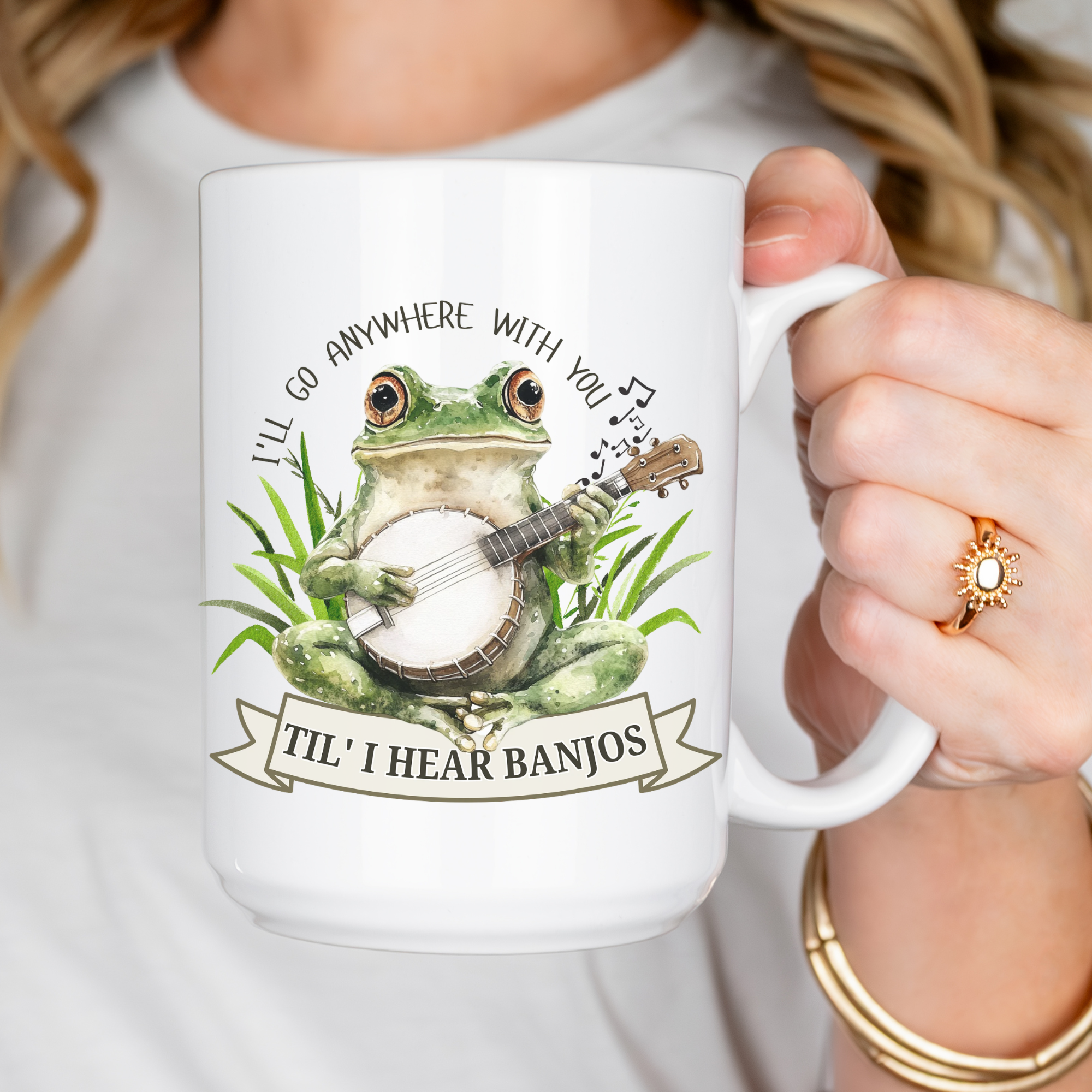 White mug with a frog playing a banjo design and text, held by a person.