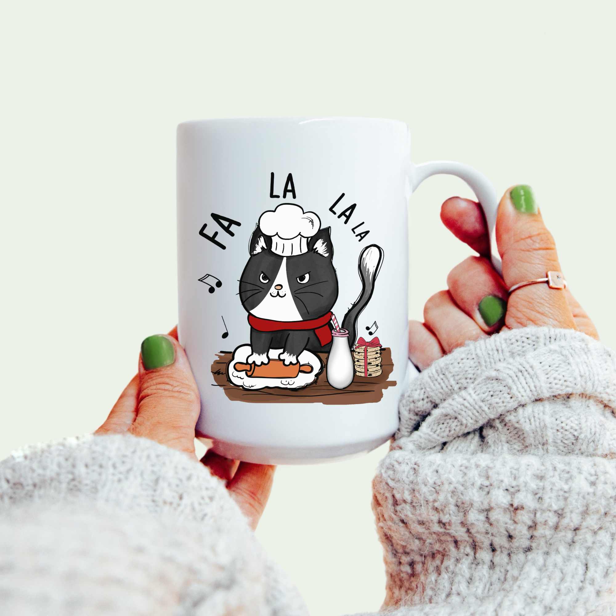 White mug with a black cat illustration and 'FA LA LA LA' text, held by a person.