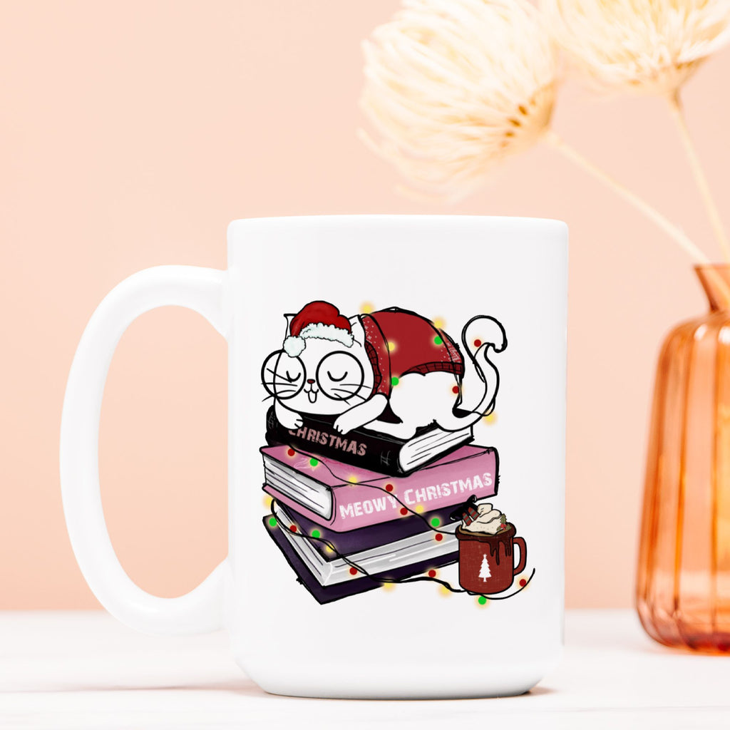 White mug with a Christmas-themed design featuring a cat, books, and a hot chocolate cup on a light pink background.
