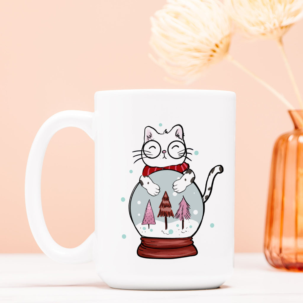 White mug with a cat illustration inside a snow globe on a light pink background