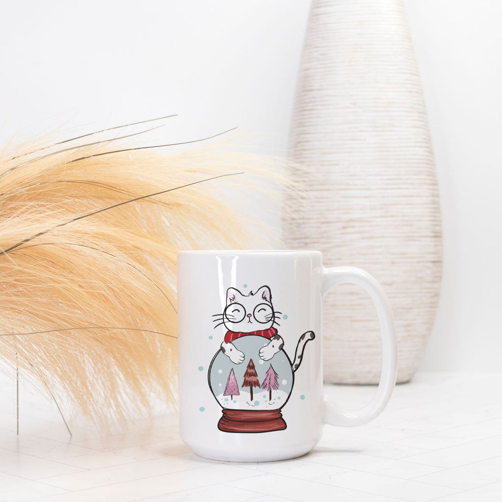 White mug with a cat illustration inside a snow globe on a white surface.