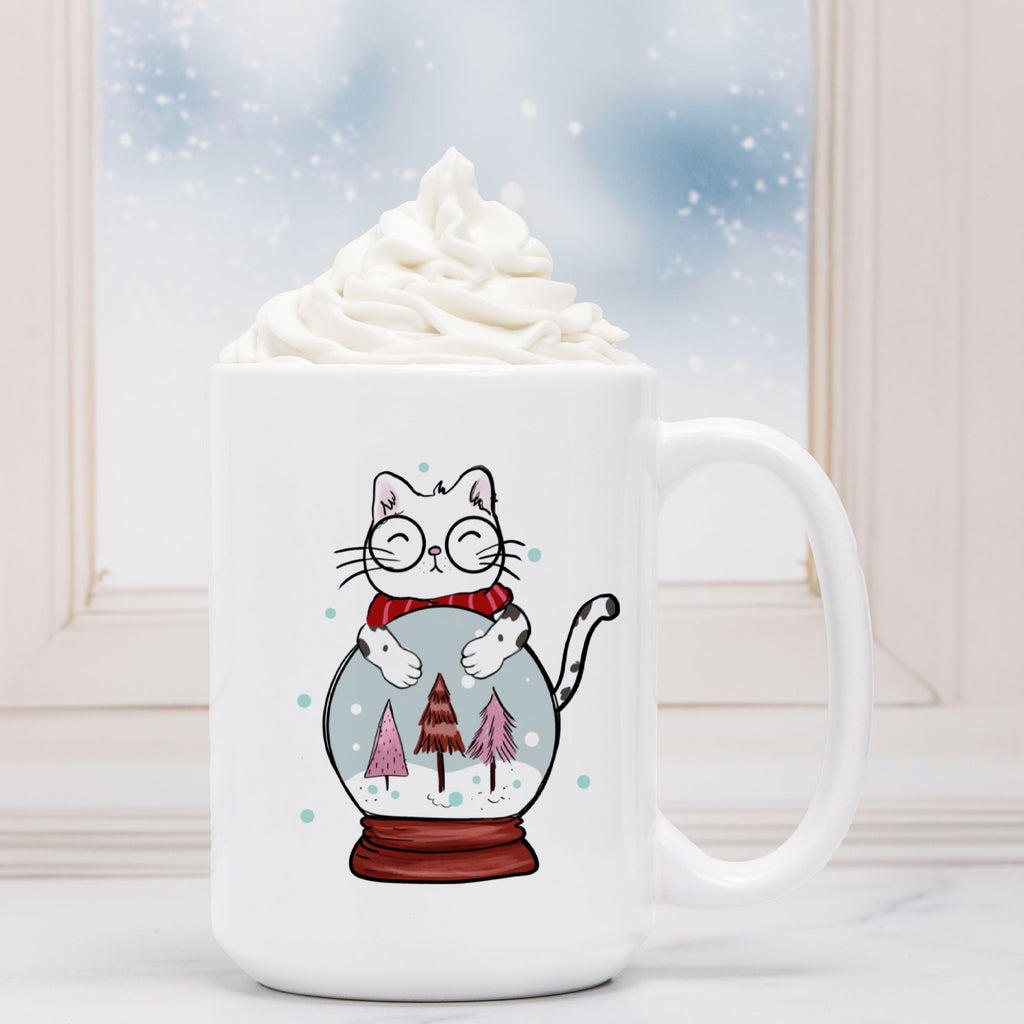 White mug with a cat illustration inside a snow globe, filled with hot chocolate and whipped cream.