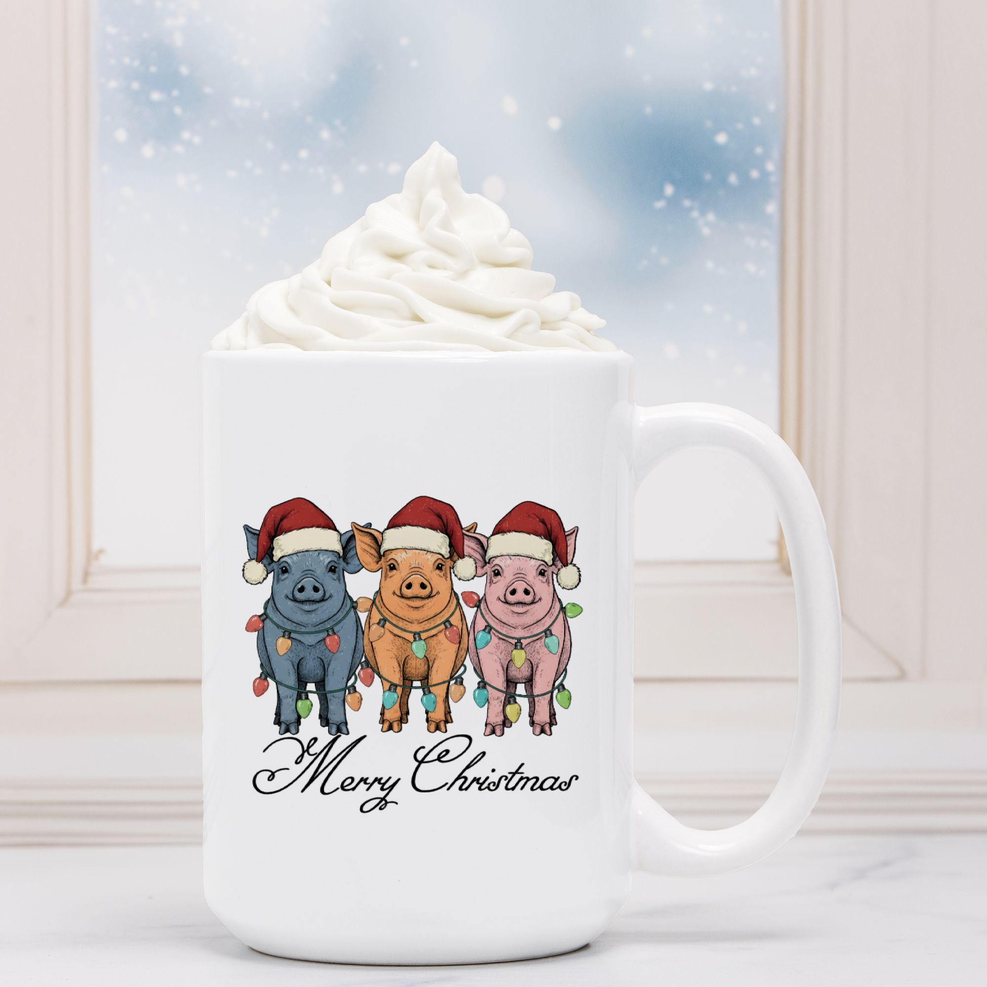 White mug with Christmas-themed design of pigs wearing hats and lights, next to a hot chocolate with whipped cream.
