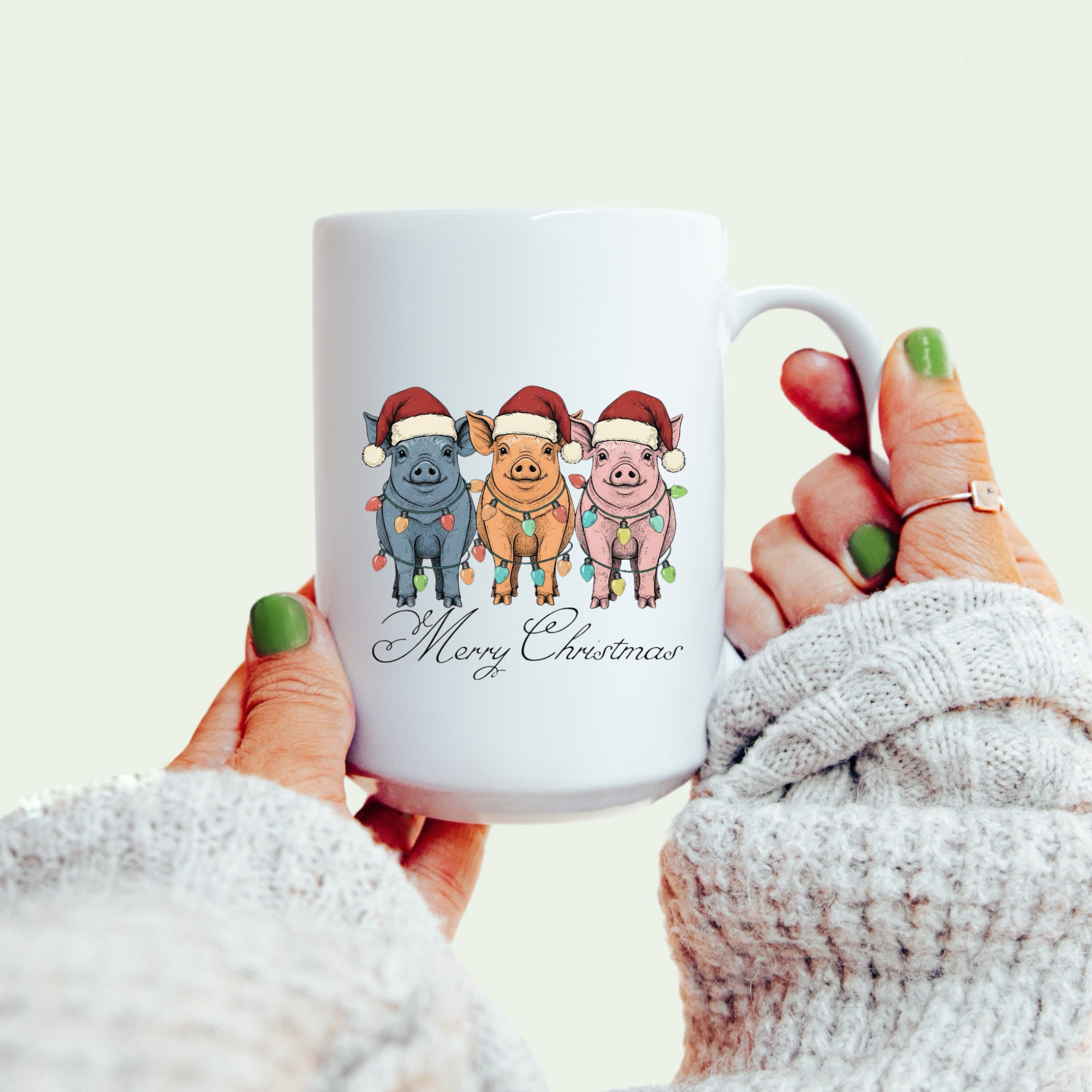 White mug with Christmas-themed design of pigs wearing hats and a 'Merry Christmas' text, held by a person.