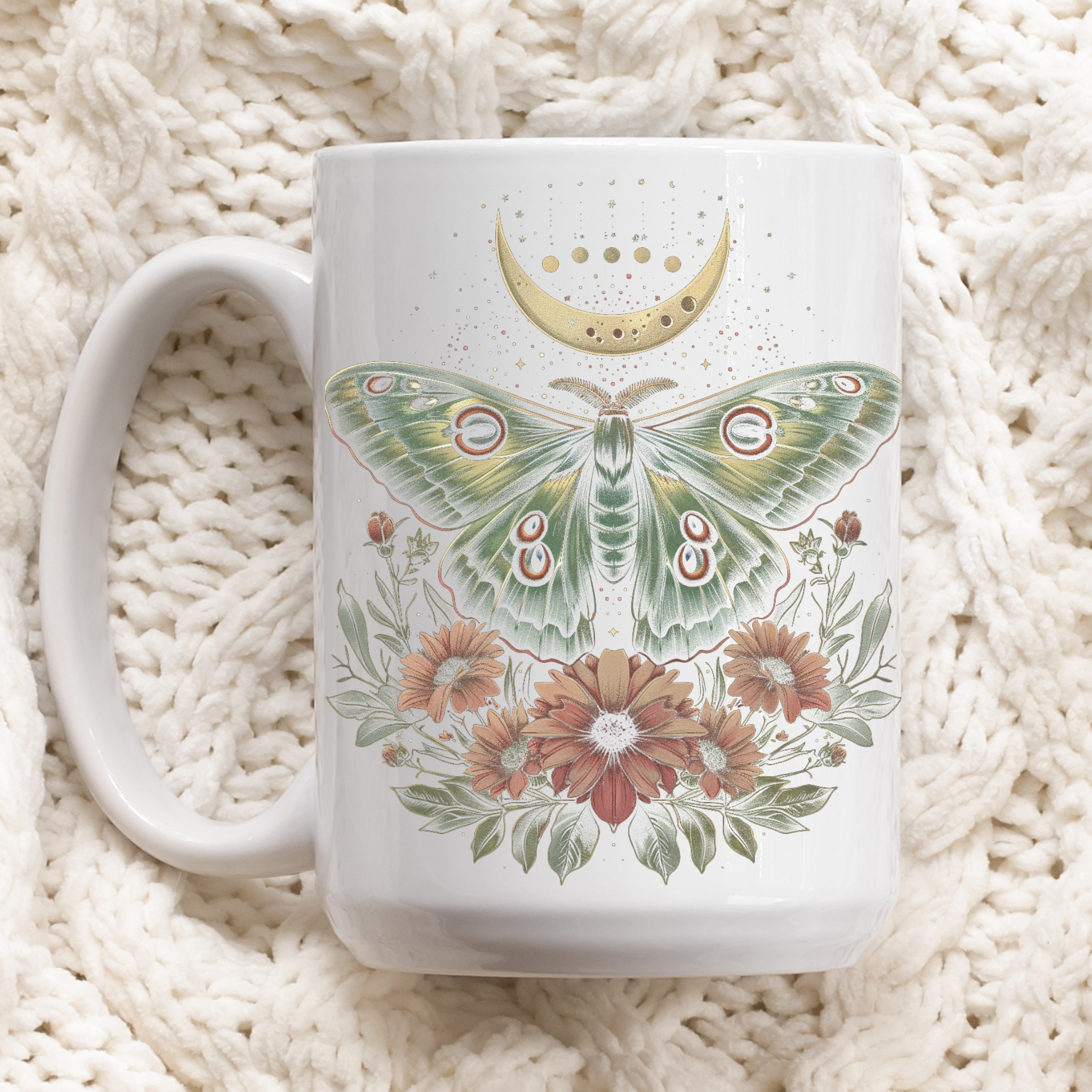 White mug with and intricate design of a cottage core Luna moth with flowers and a partial celestial moon in colors of green, gold, and pink. Laying down.