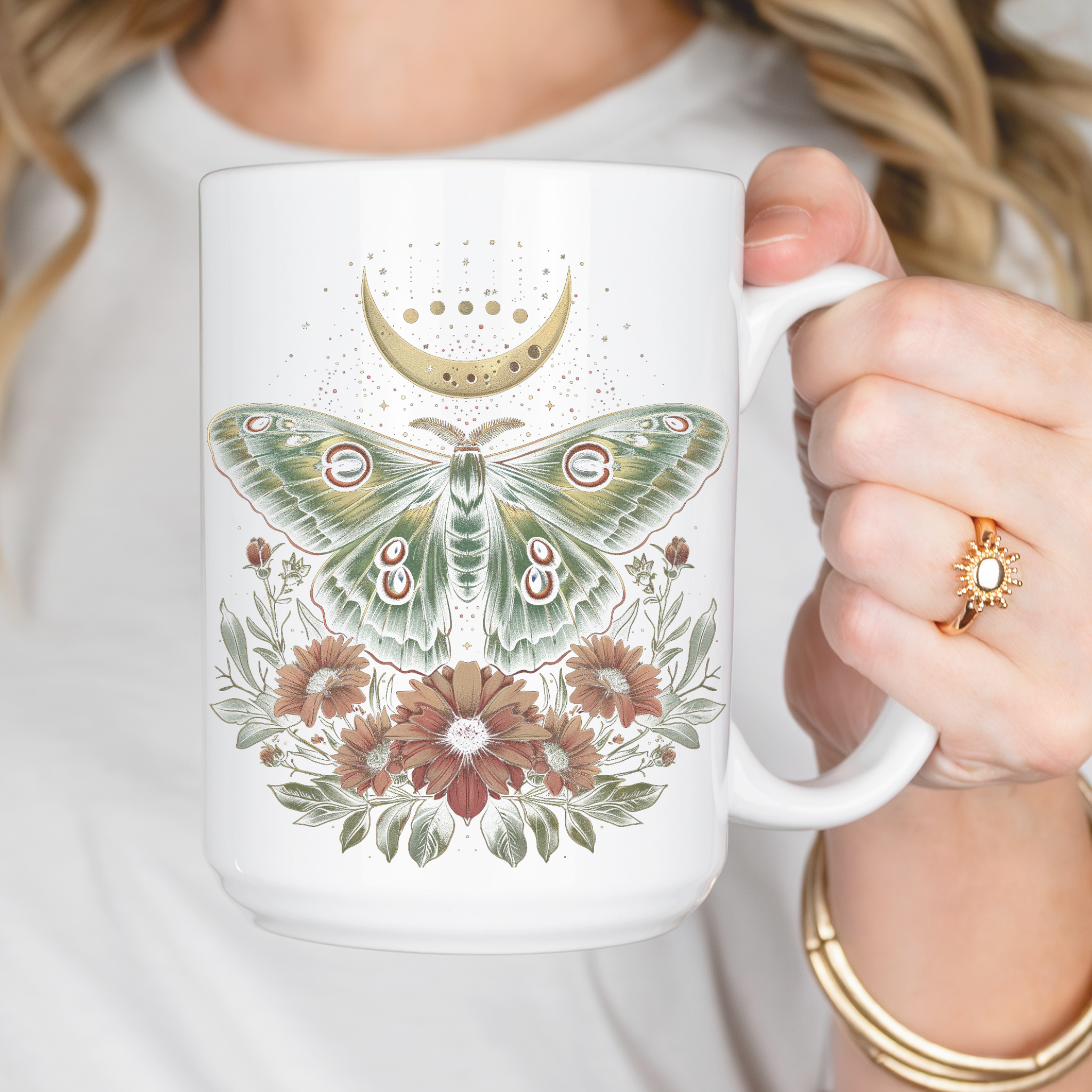 White mug with and intricate design of a cottage core Luna moth with flowers and a partial celestial moon in colors of green, gold, and pink.