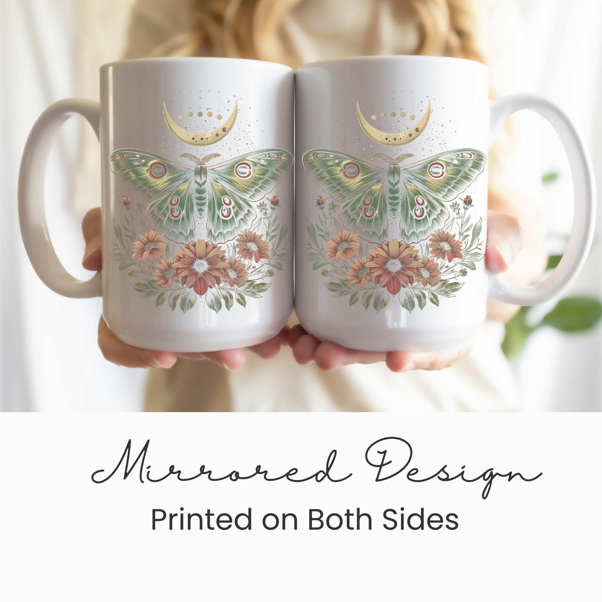 A person holding two White mugs with and intricate design of a cottage core Luna moth with flowers and a partial celestial moon in colors of green, gold, and pink.