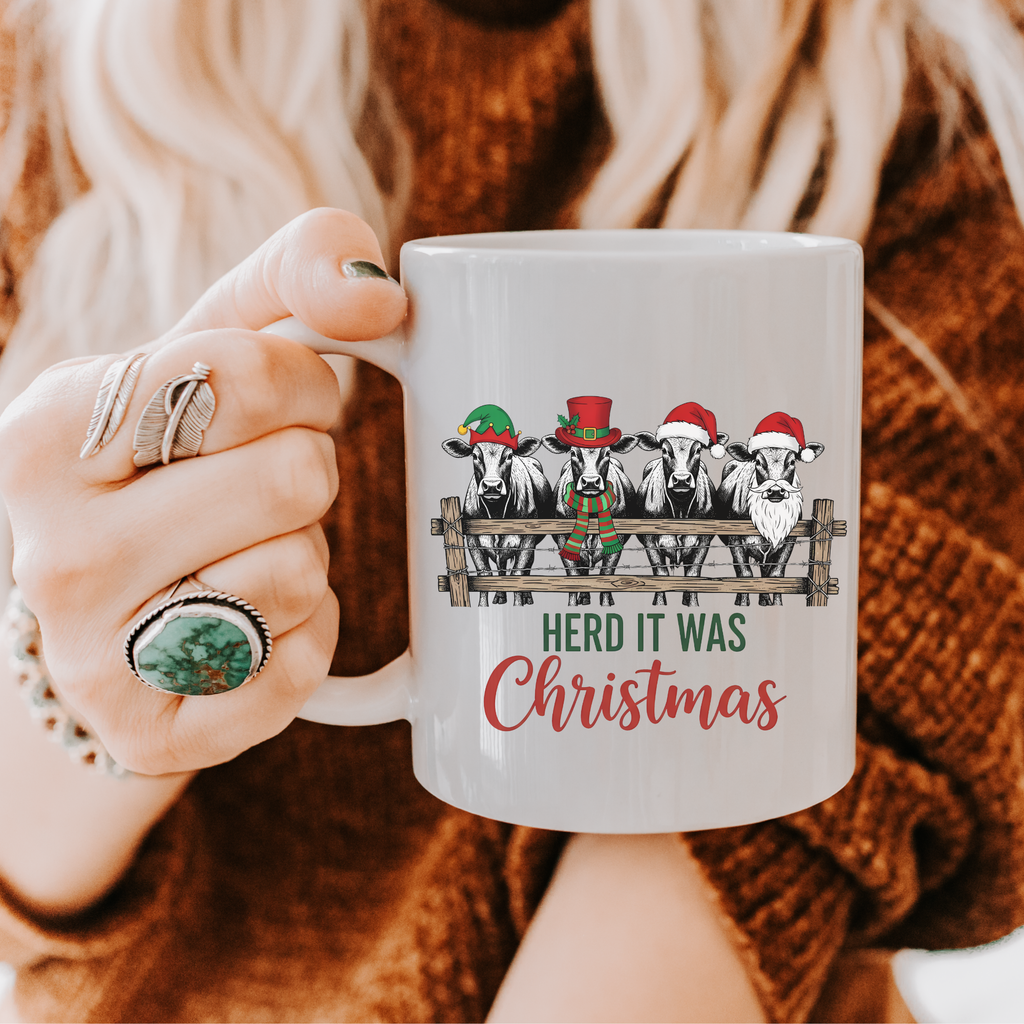 Person holding a mug with Christmas-themed design featuring cows and Santa hats.