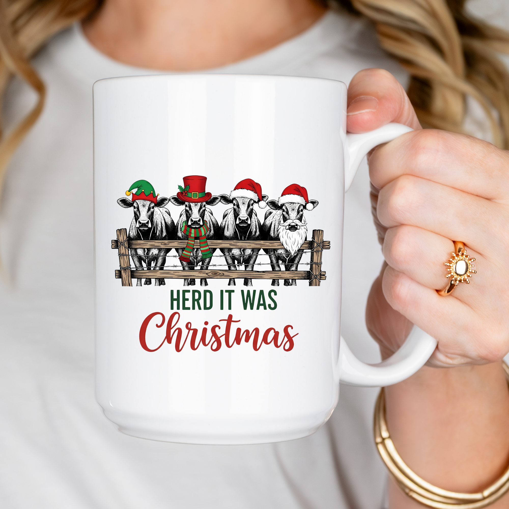 Person holding a mug with Christmas-themed design of cows wearing Santa hats and text 'HERD IT WAS Christmas'.