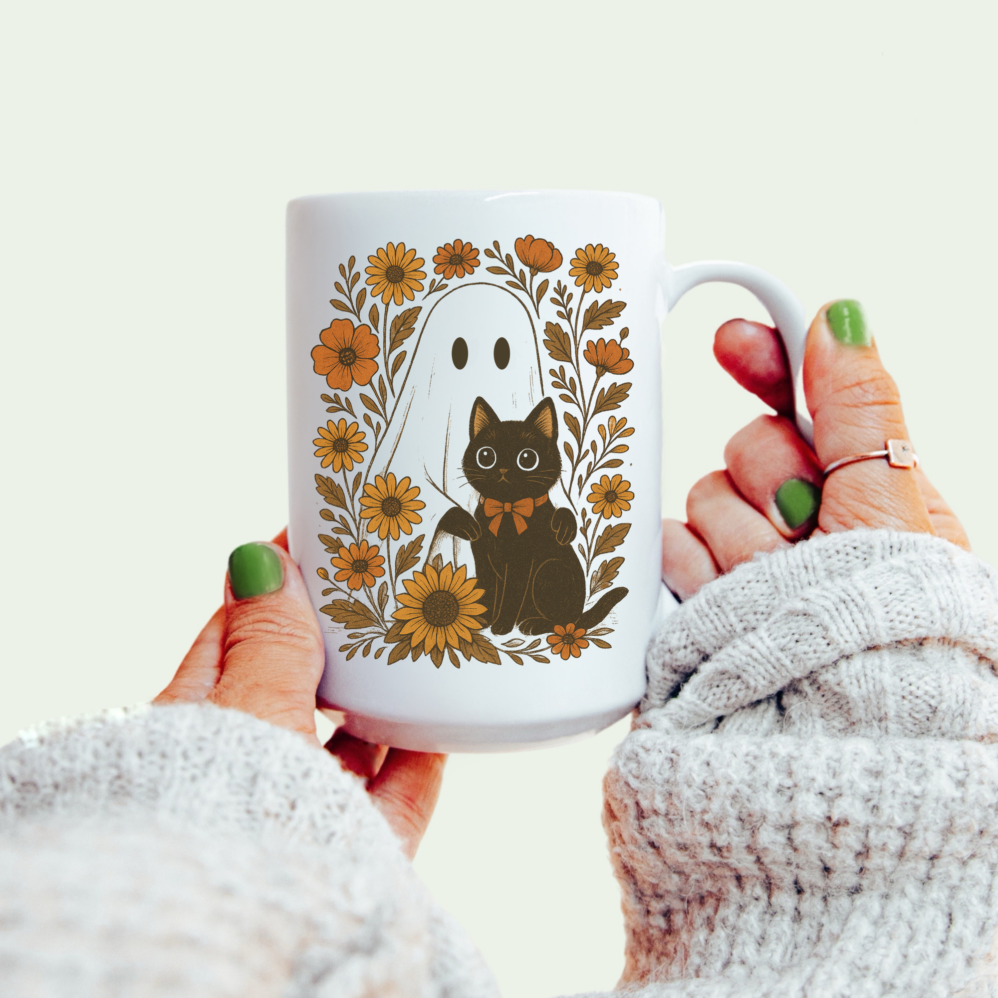 White mug with a black cat and floral design held by a person wearing a white sweater.