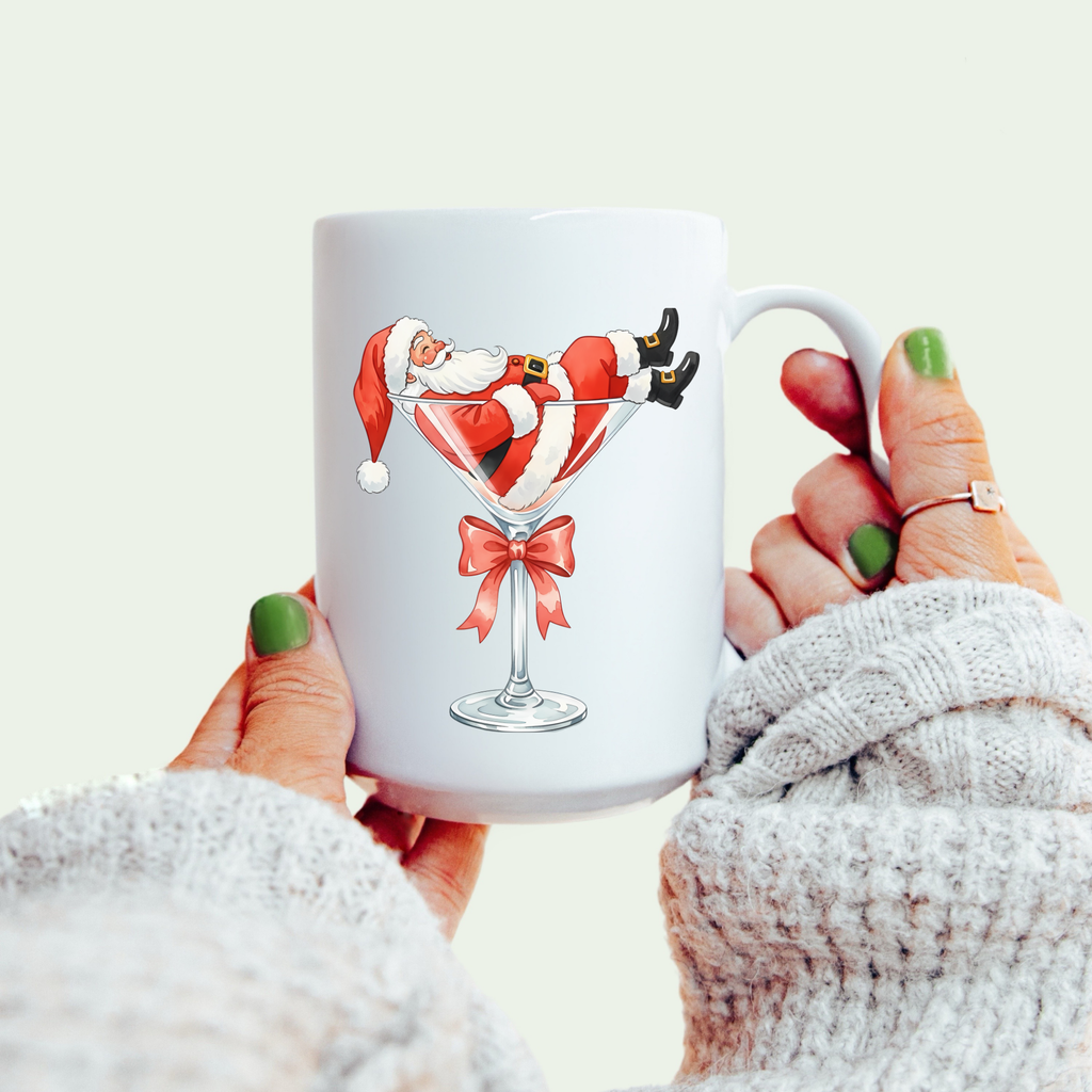 White mug with Santa Claus design held by a person wearing a white sweater.