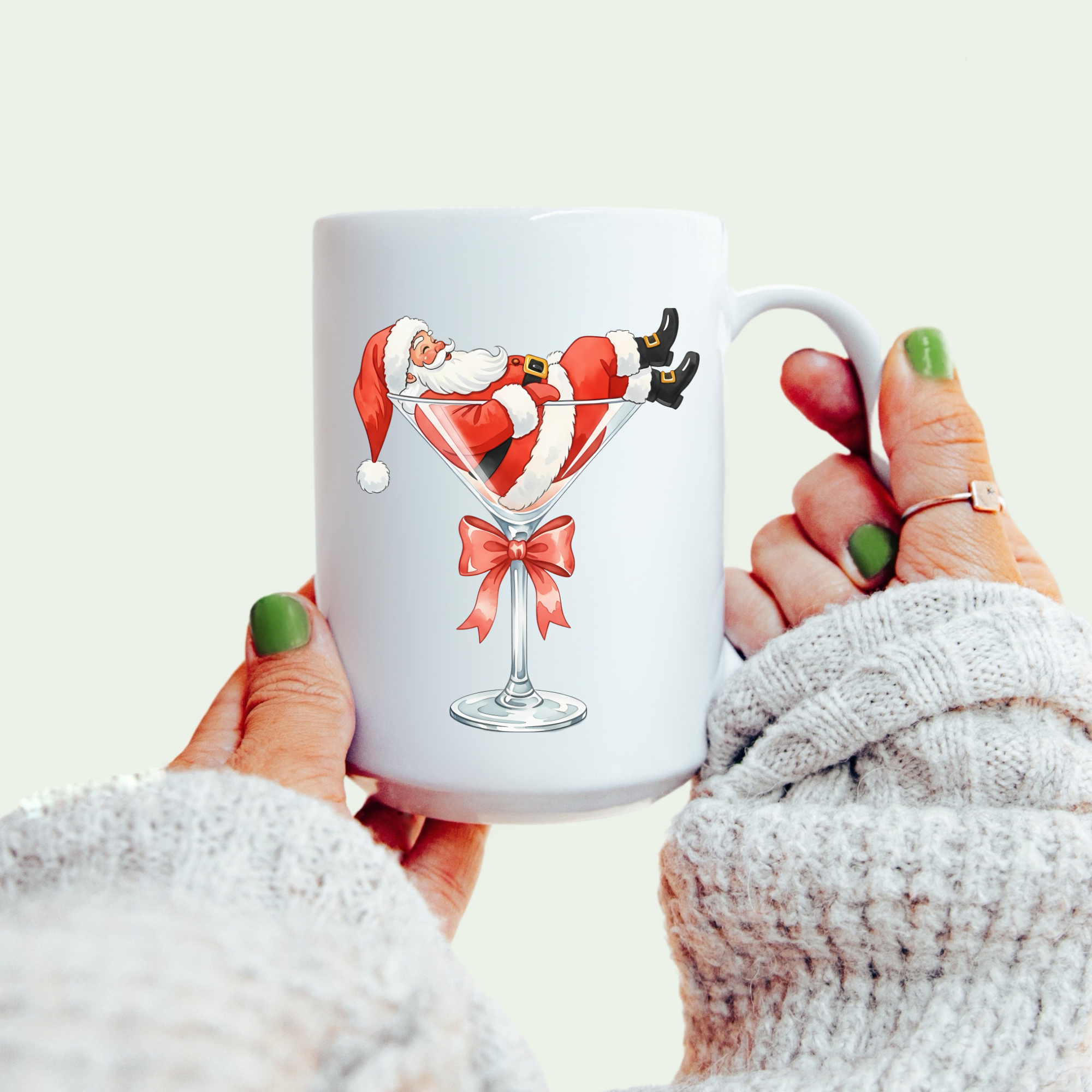 White mug with Santa Claus design held by a person wearing a white sweater.