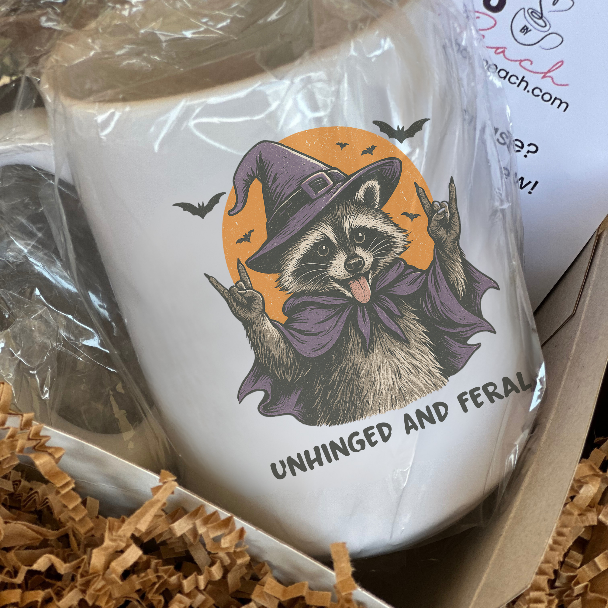 Mug with raccoon wearing a witch hat design and text 'Unhinged and Feral' in a box.