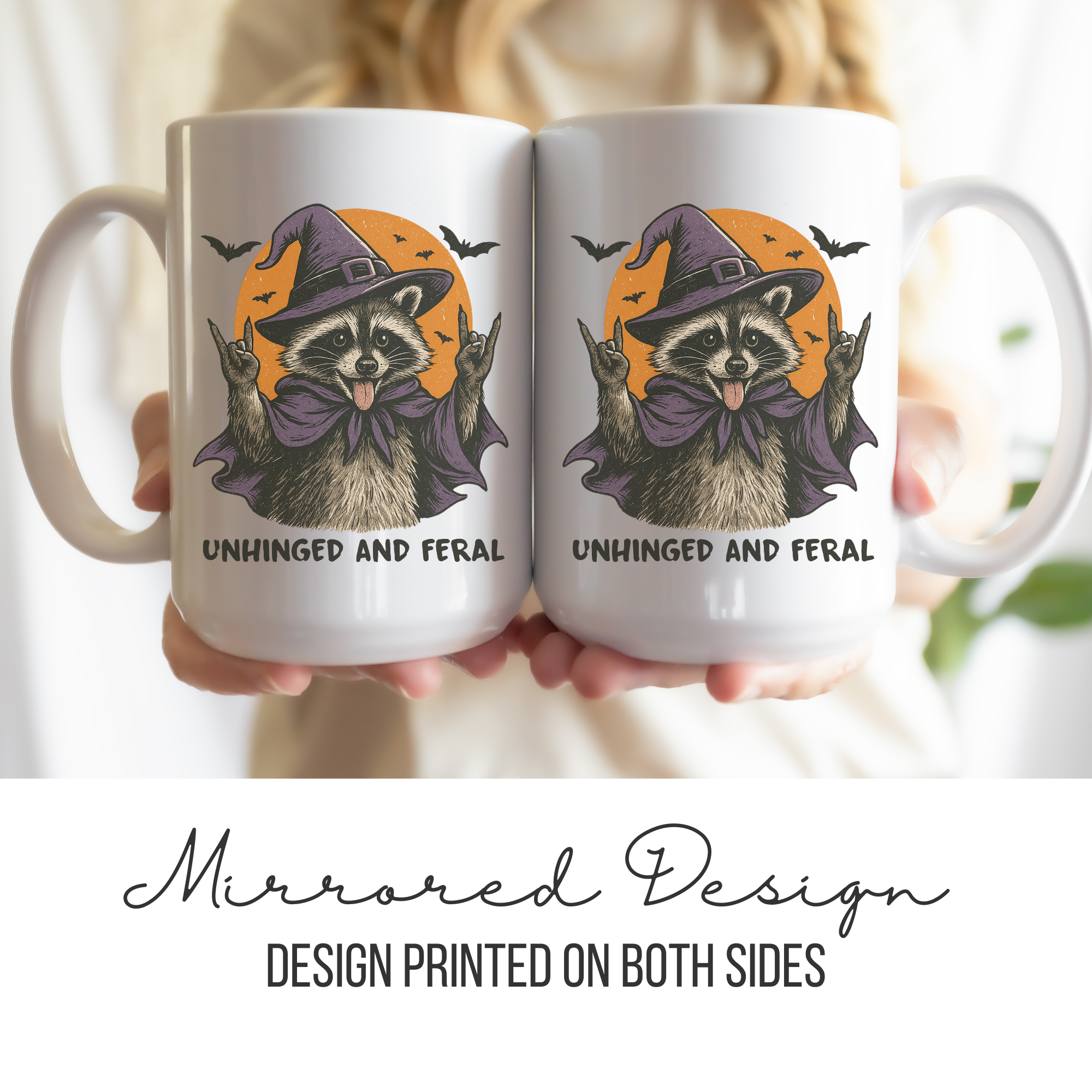 Two white mugs with a mirrored design of a raccoon wearing a witch hat and text 'Unhinged and Feral' held by a person.