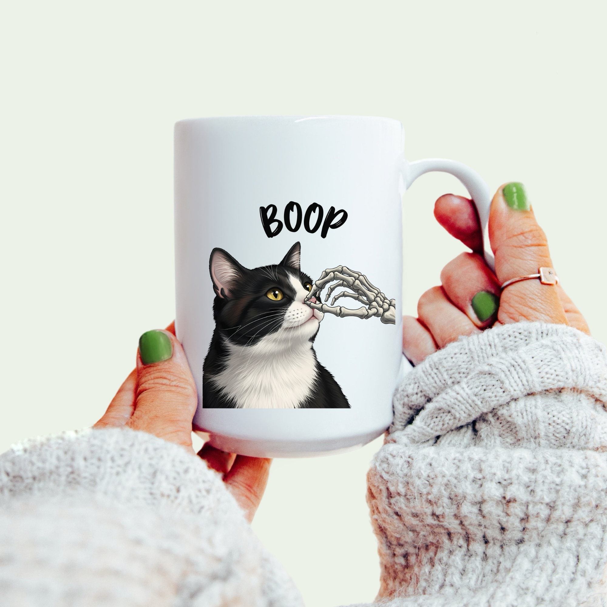 White mug with a black and white cat illustration and 'BOOP' text, held by a person.