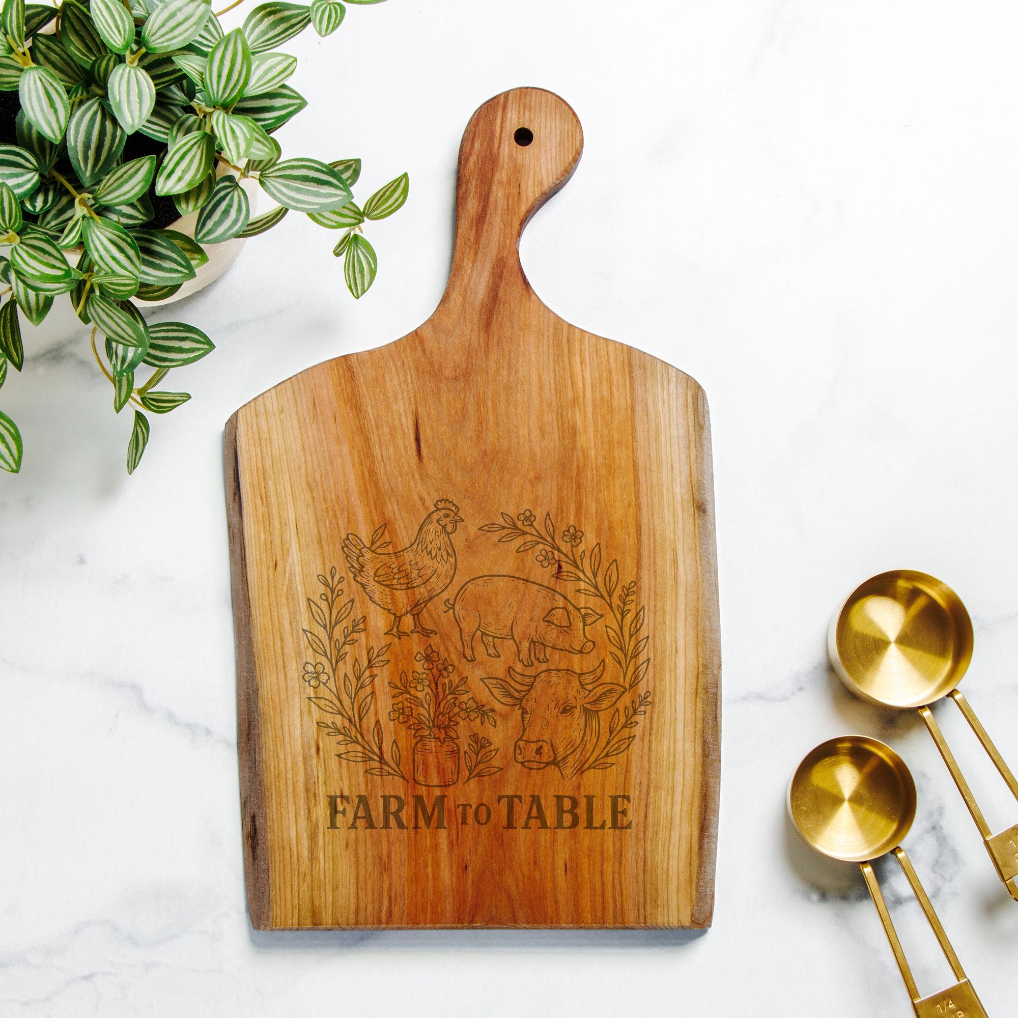 Wooden cutting board with 'Farm to Table' engraving on a marble surface with gold measuring spoons and a plant.