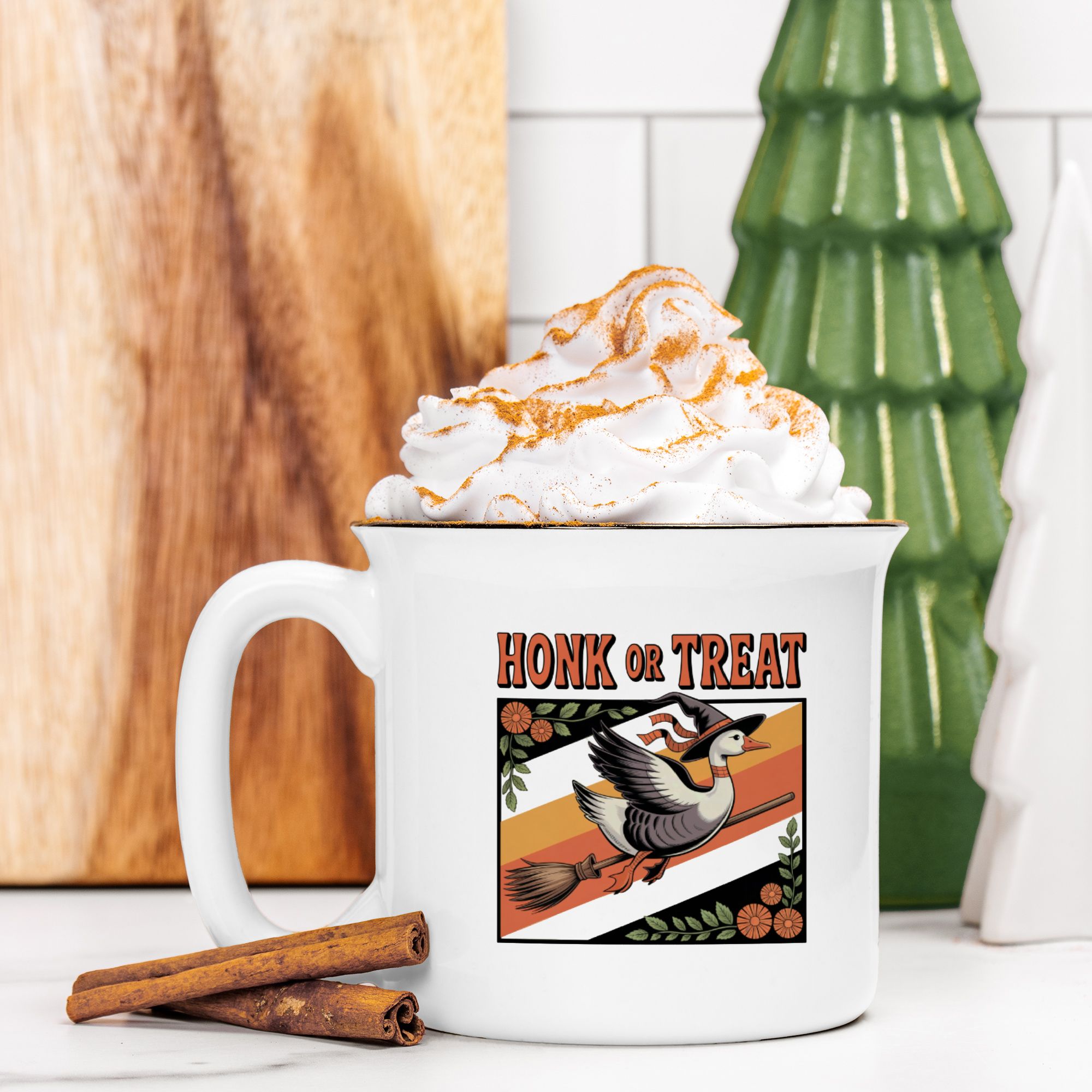 White mug with 'Honk or Treat' design featuring a bird, topped with whipped cream and a cinnamon stick on a wooden surface.