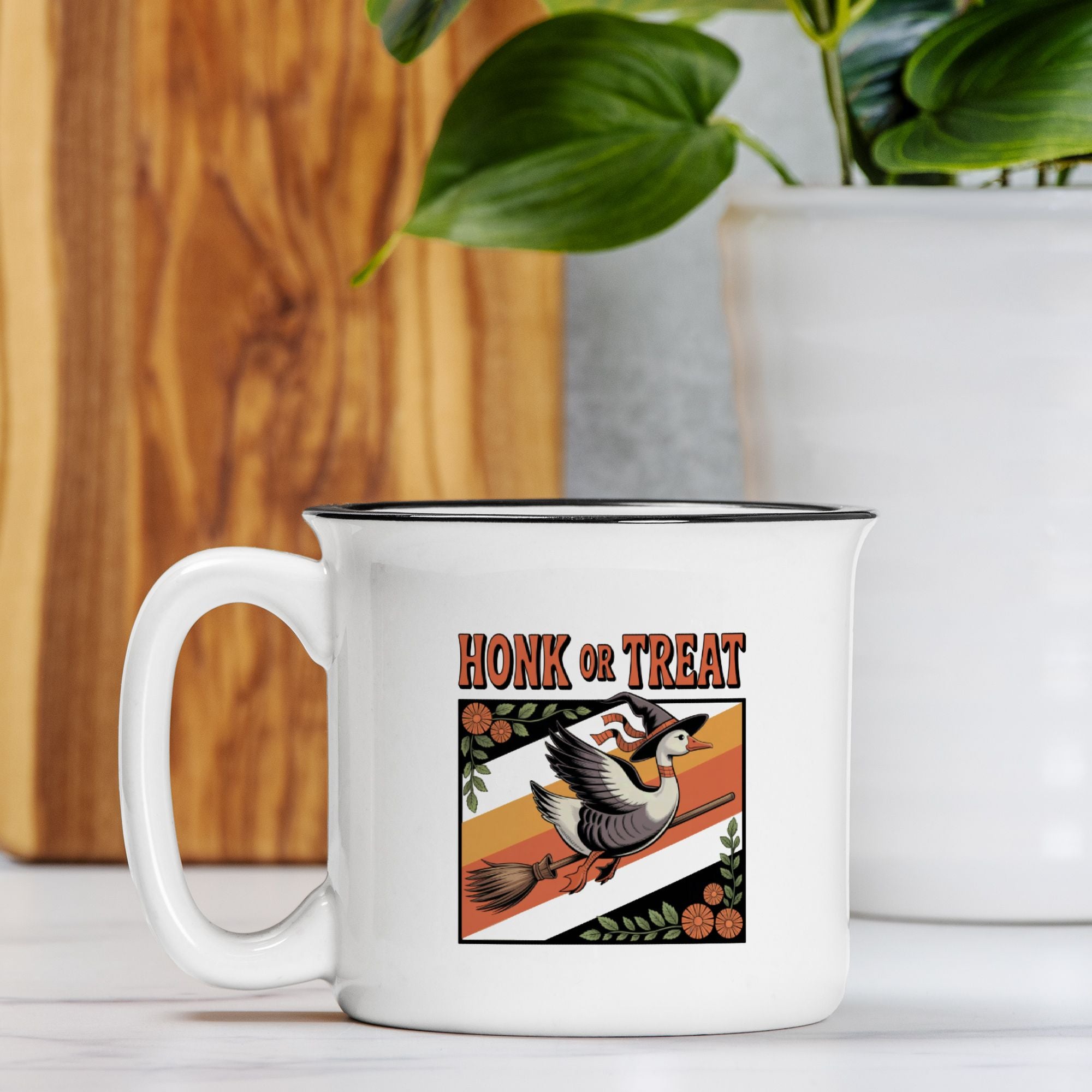 White mug with 'Honk or Treat' design featuring a goose and broomstick, placed on a wooden surface with a plant in the background.