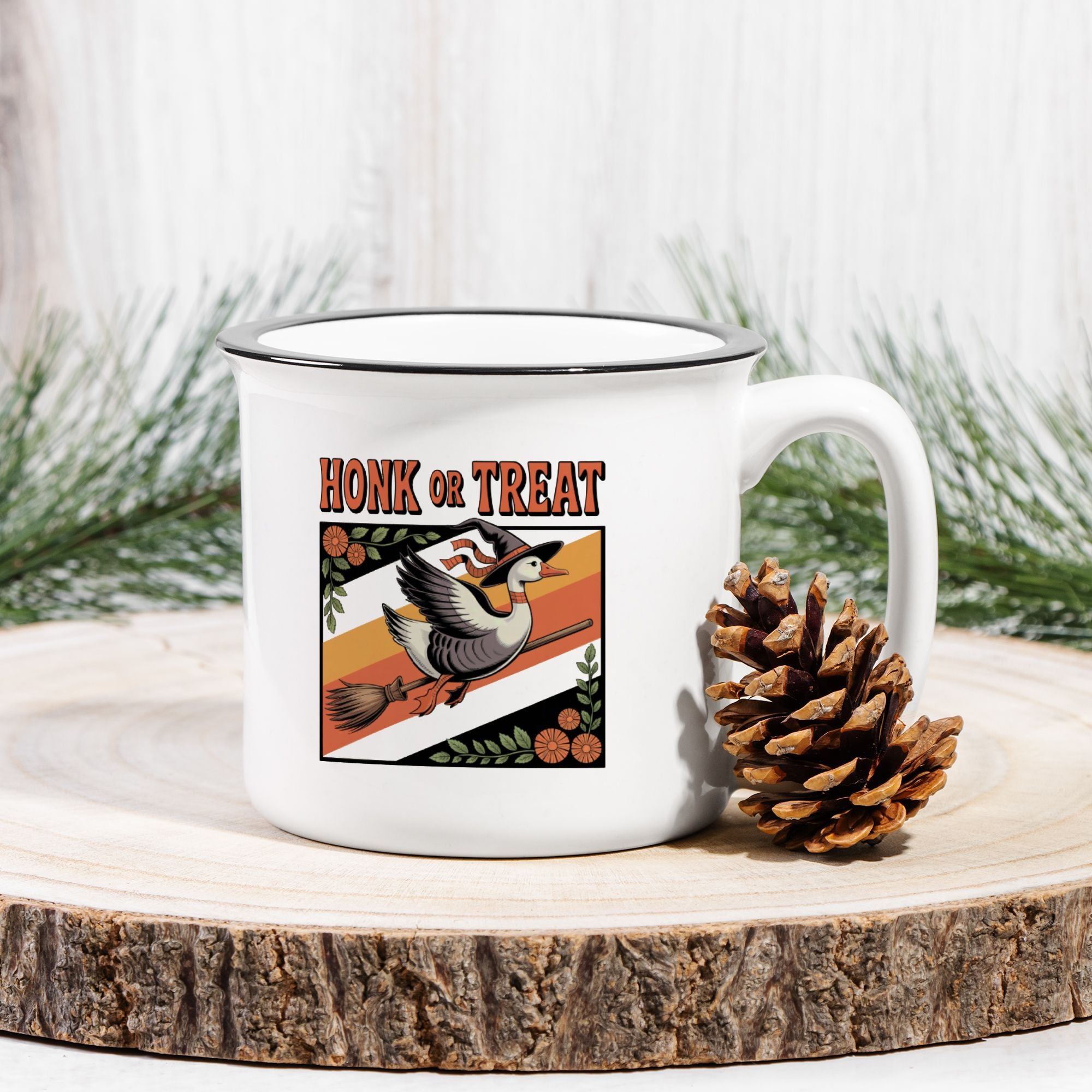 White mug with 'Honk or Treat' design featuring a goose and broomstick, on a wooden surface with a pine cone and greenery.