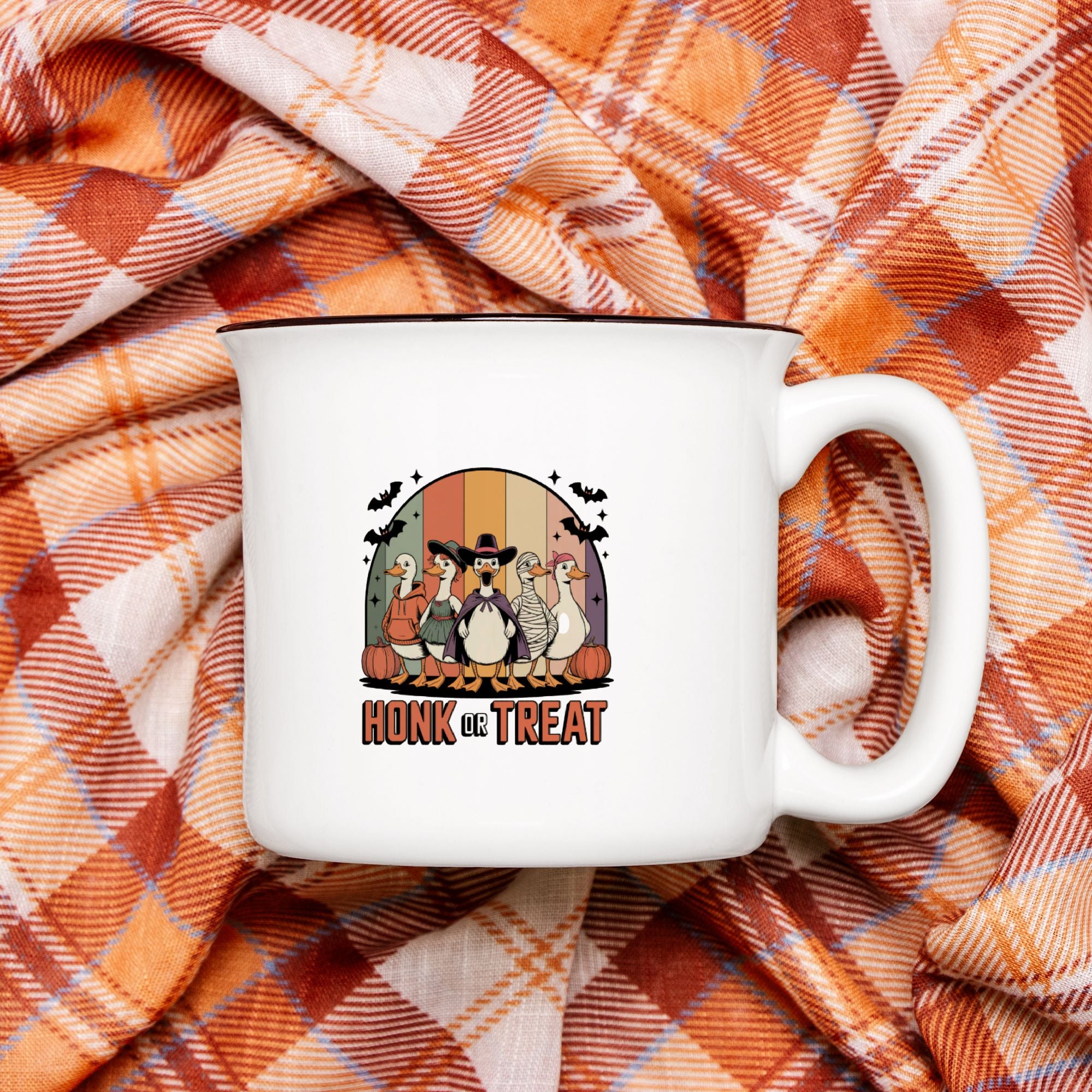 White camping mug with a graphic design of Halloween dressed geese on an orange plaid fabric background.