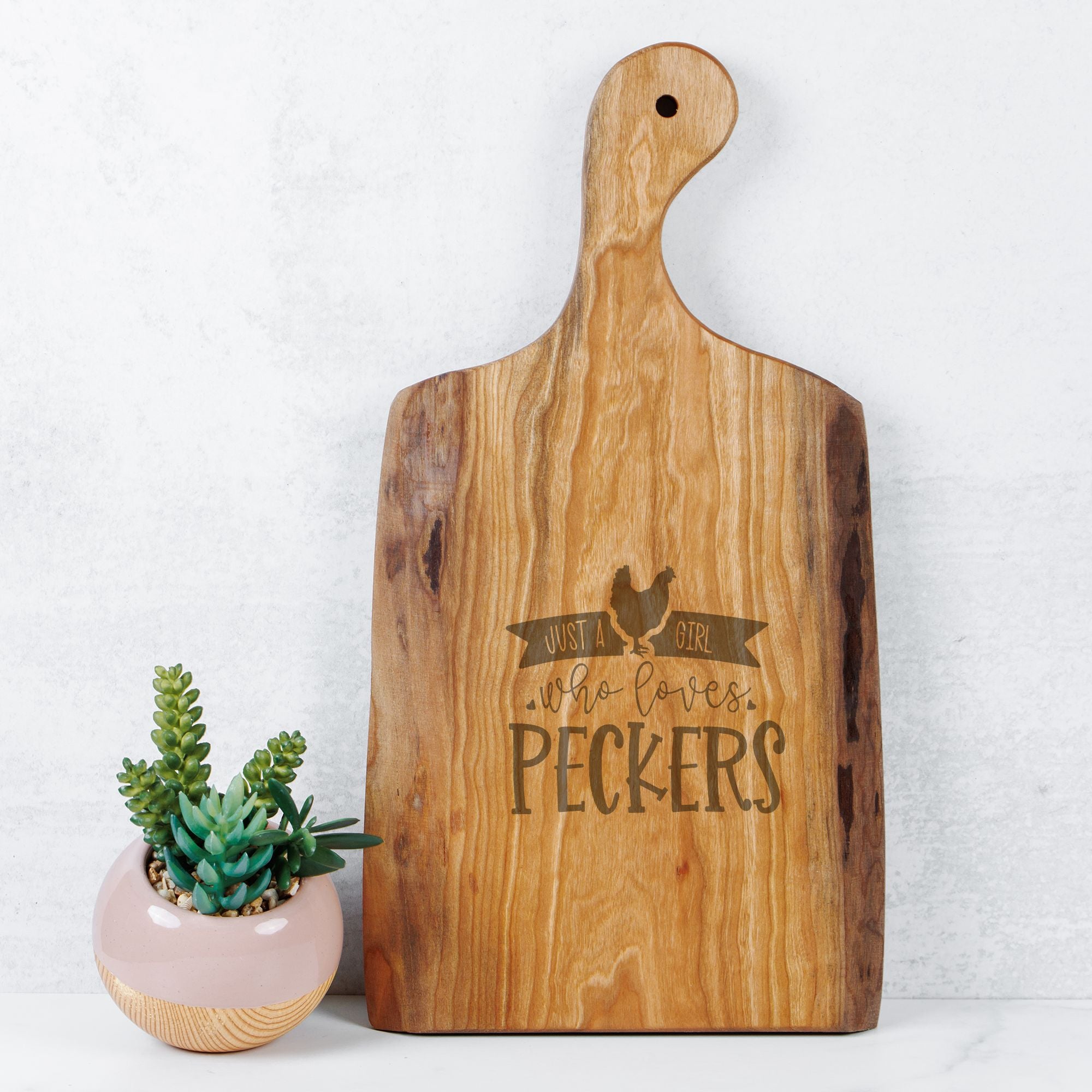 Wooden cutting board with engraved text next to a small potted plant on a light background