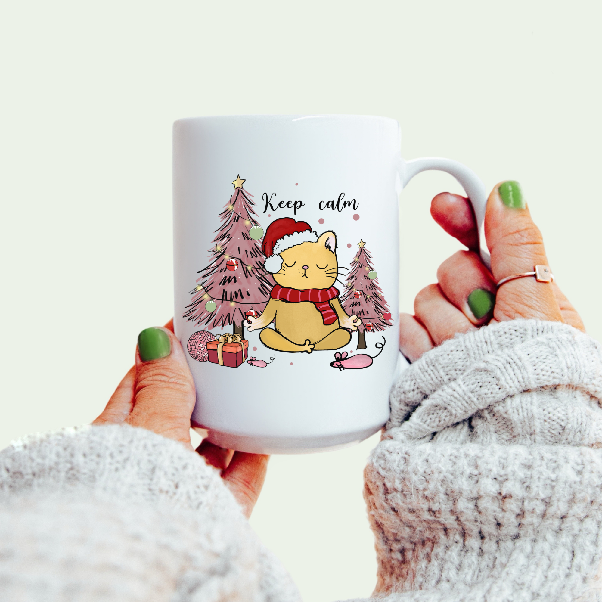White mug with a Christmas-themed design of a cat and trees, held by a person.