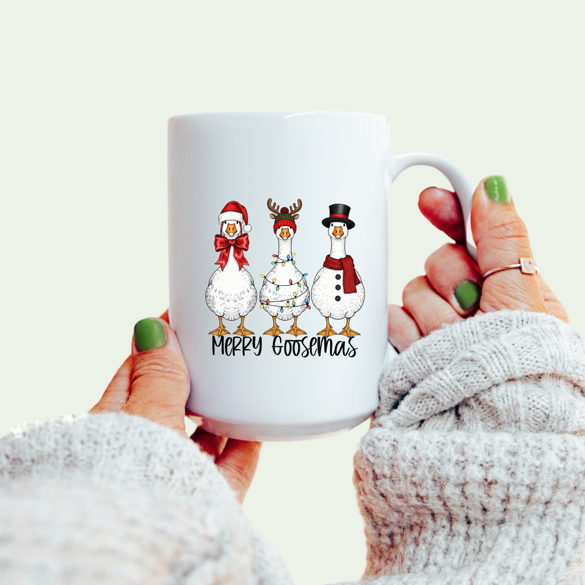 White mug with Christmas-themed design of geese and text 'Merry Goodsmas' held by a person.