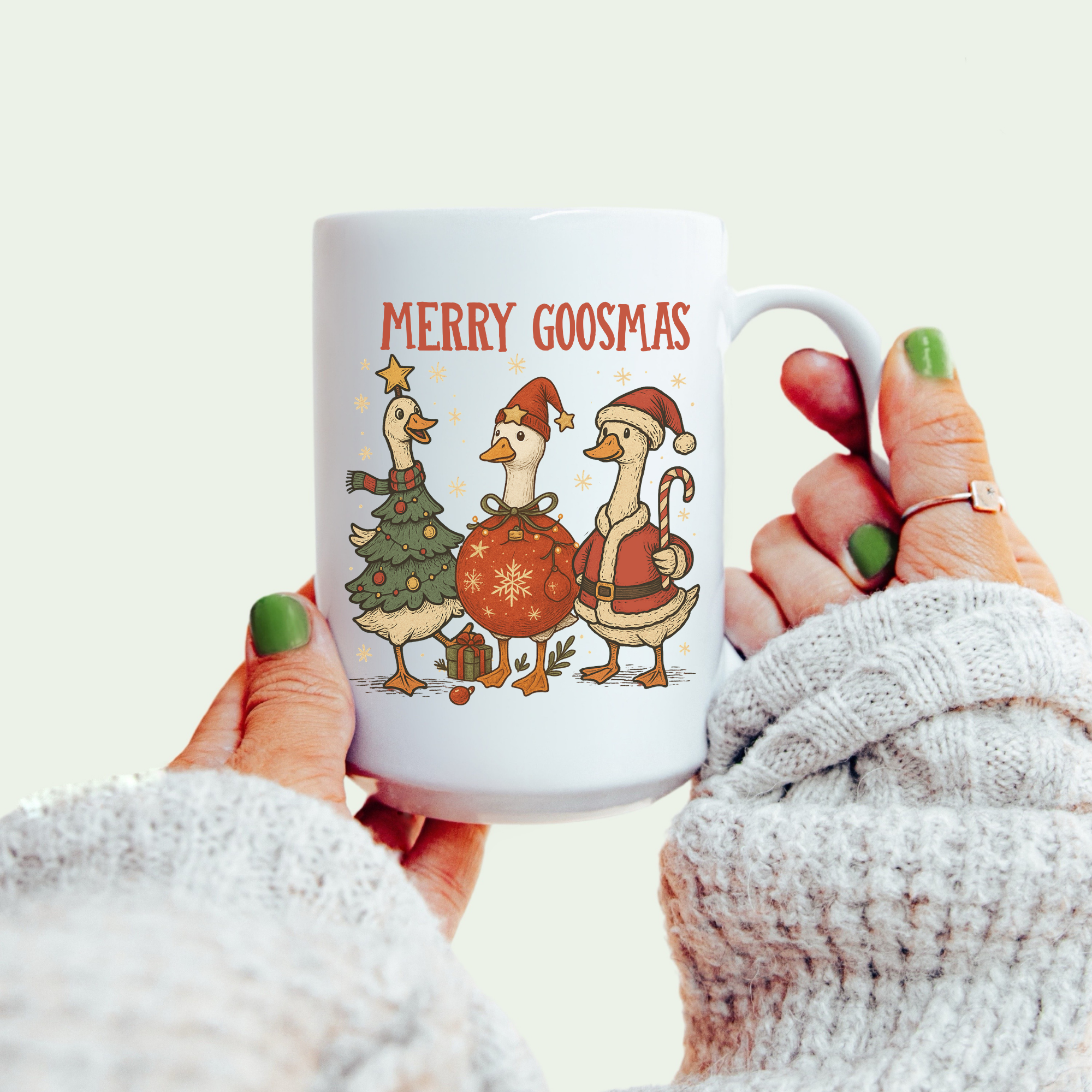 Mug with 'Merry Goosmas' design featuring cartoon geese, held by a person wearing a white sweater.