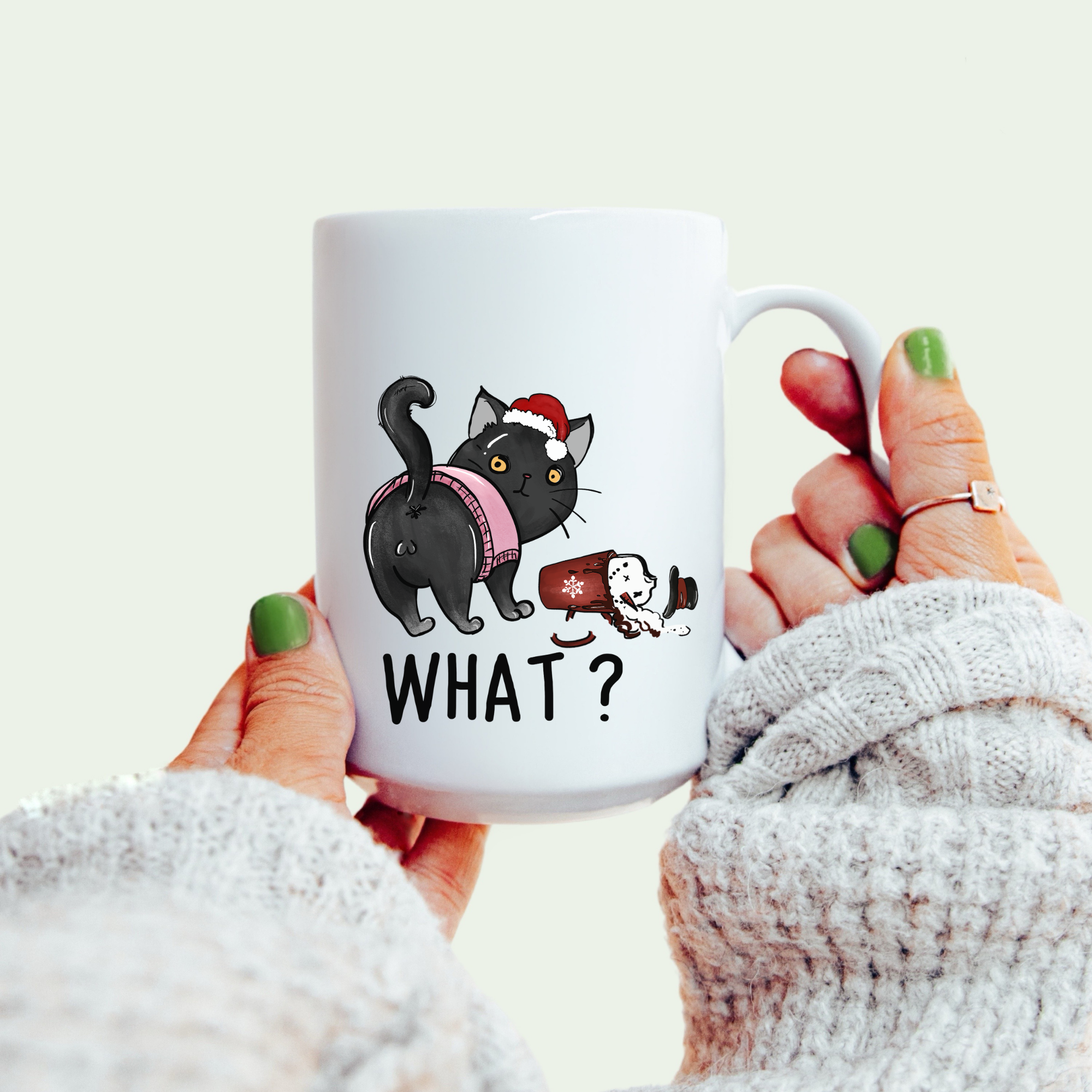 White mug with a Christmas black cat design and text 'What?' held by a person wearing a white sweater.