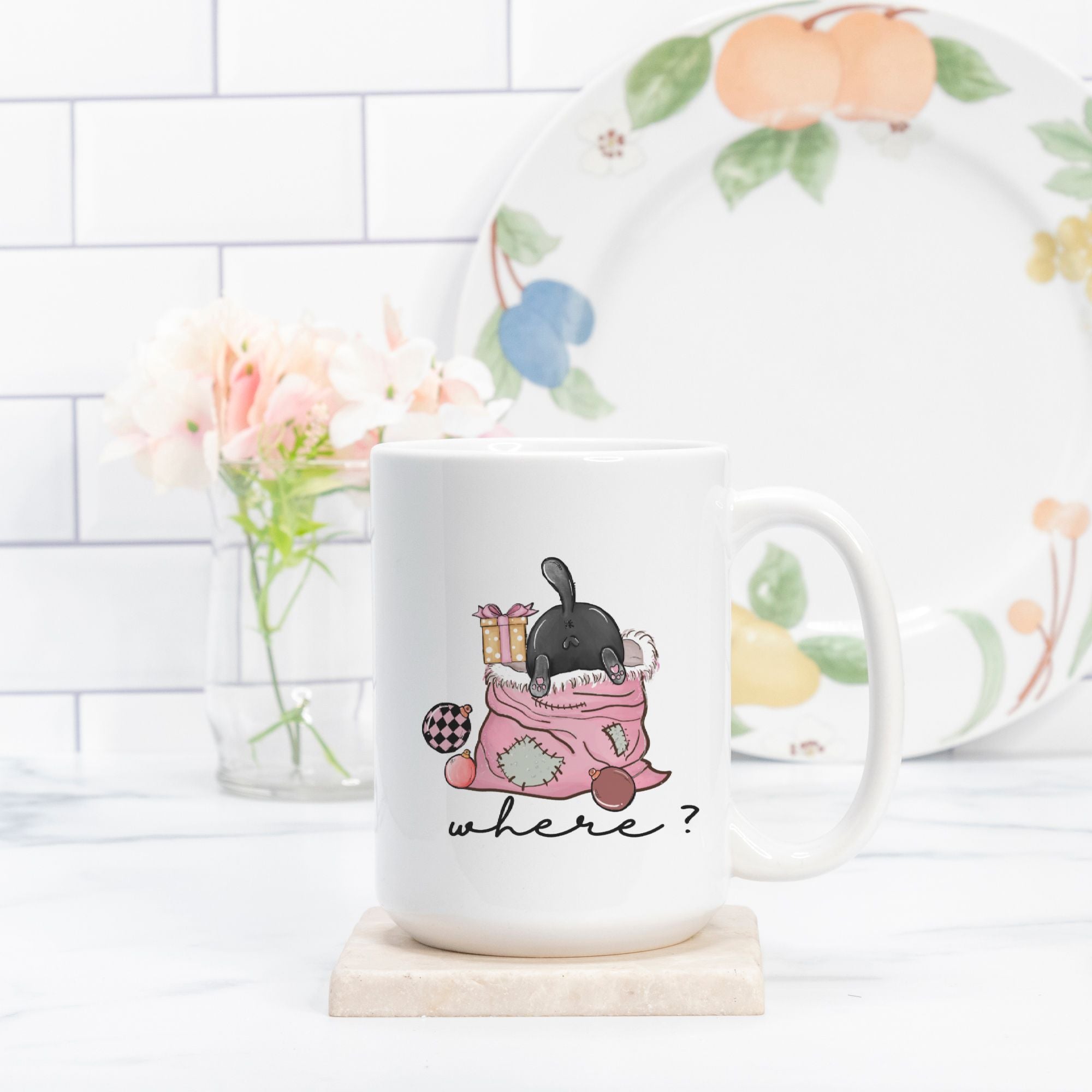 White mug with a cartoon cat design and 'where?' text, placed on a wooden coaster with a floral-patterned plate in the background.