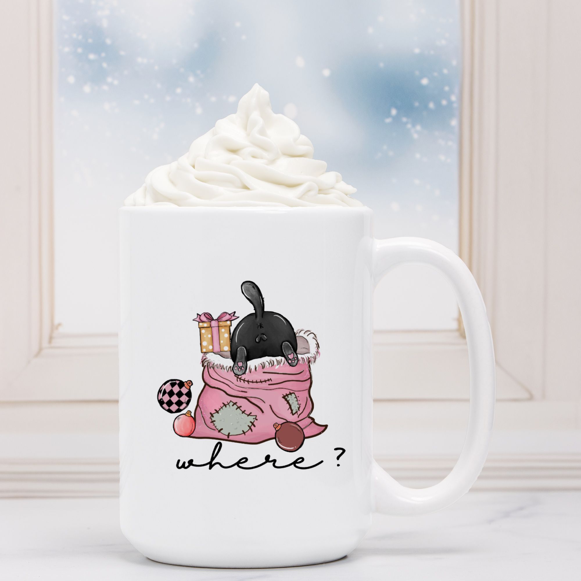 White mug with a cartoon black cat design and text 'Where?', placed in front of a hot chocolate with whipped cream.