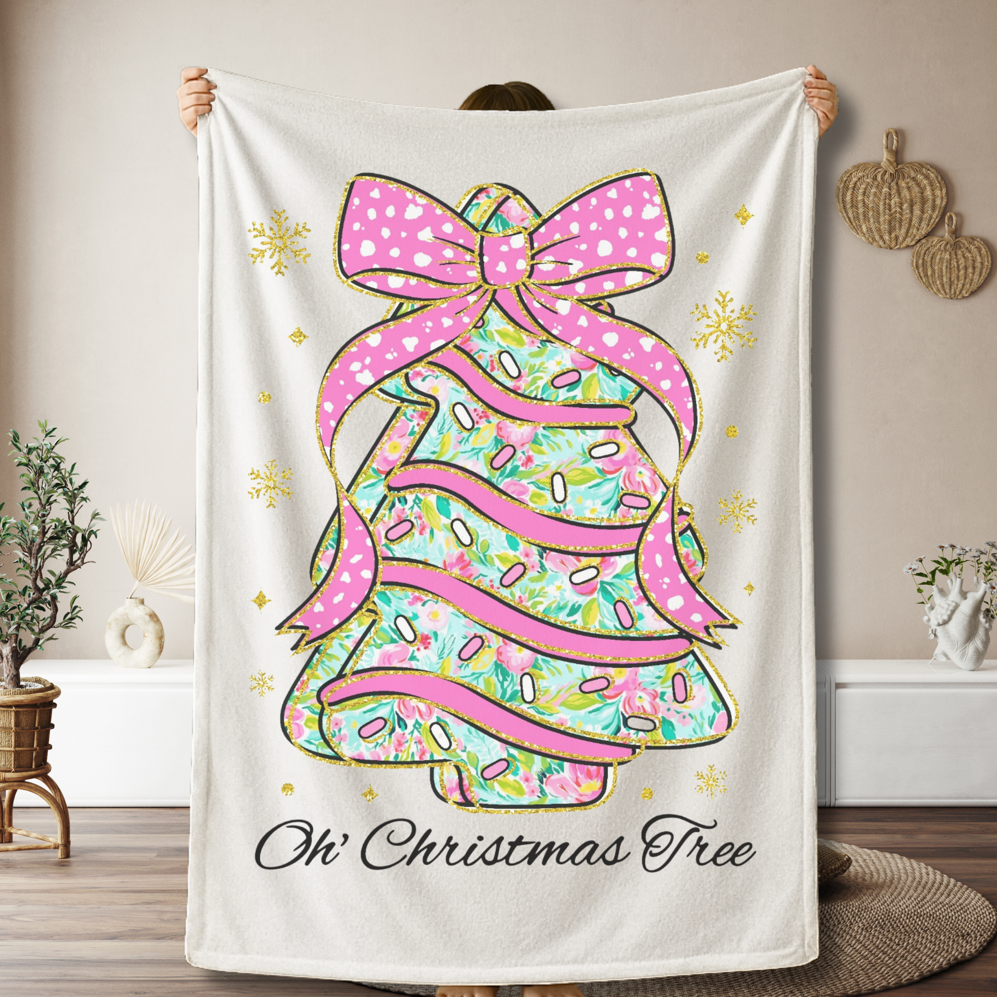 Blanket with a colorful Christmas tree cake design with a pink coquette bow and text 'Oh' Christmas Tree'  held by a person in a room.