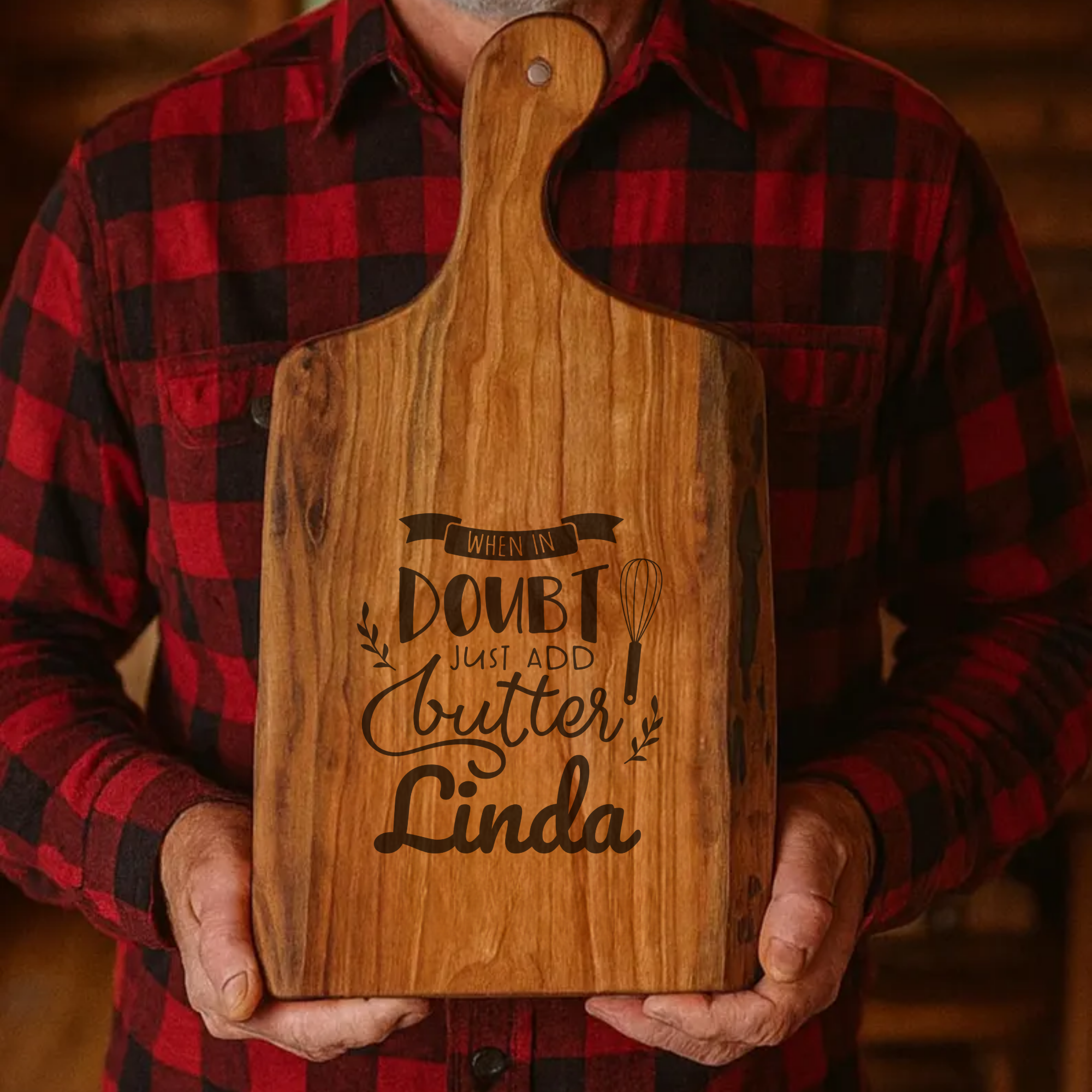 Person holding a wooden cutting board with engraved text, wearing a red and black plaid shirt.