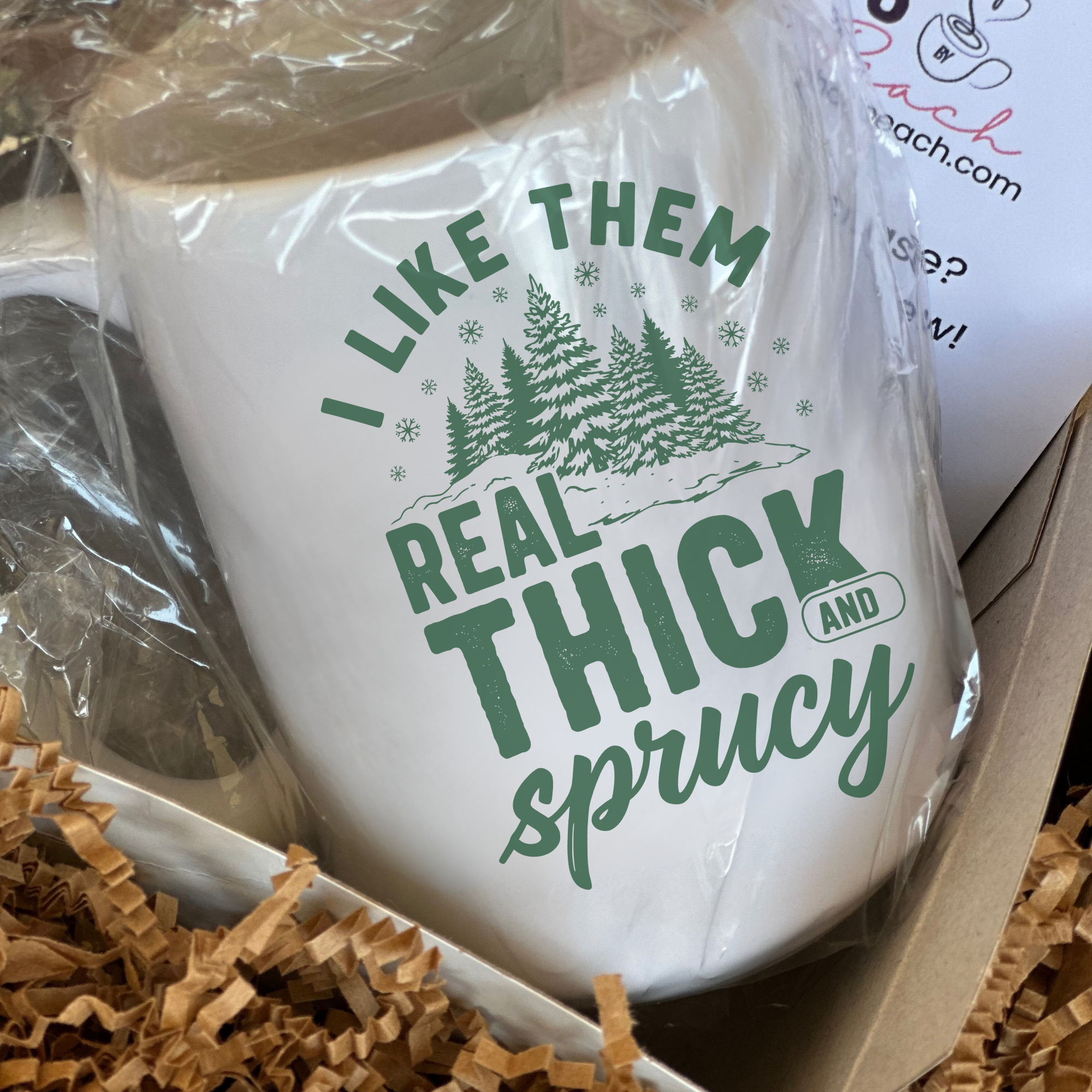 White mug with green text and forest design in a box with brown tissue paper
