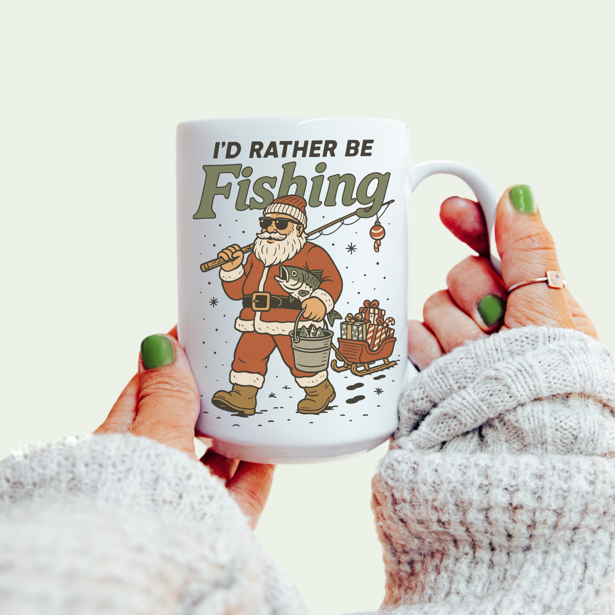 Mug with Santa Claus illustration and 'I'd Rather Be Fishing' text held by a person.