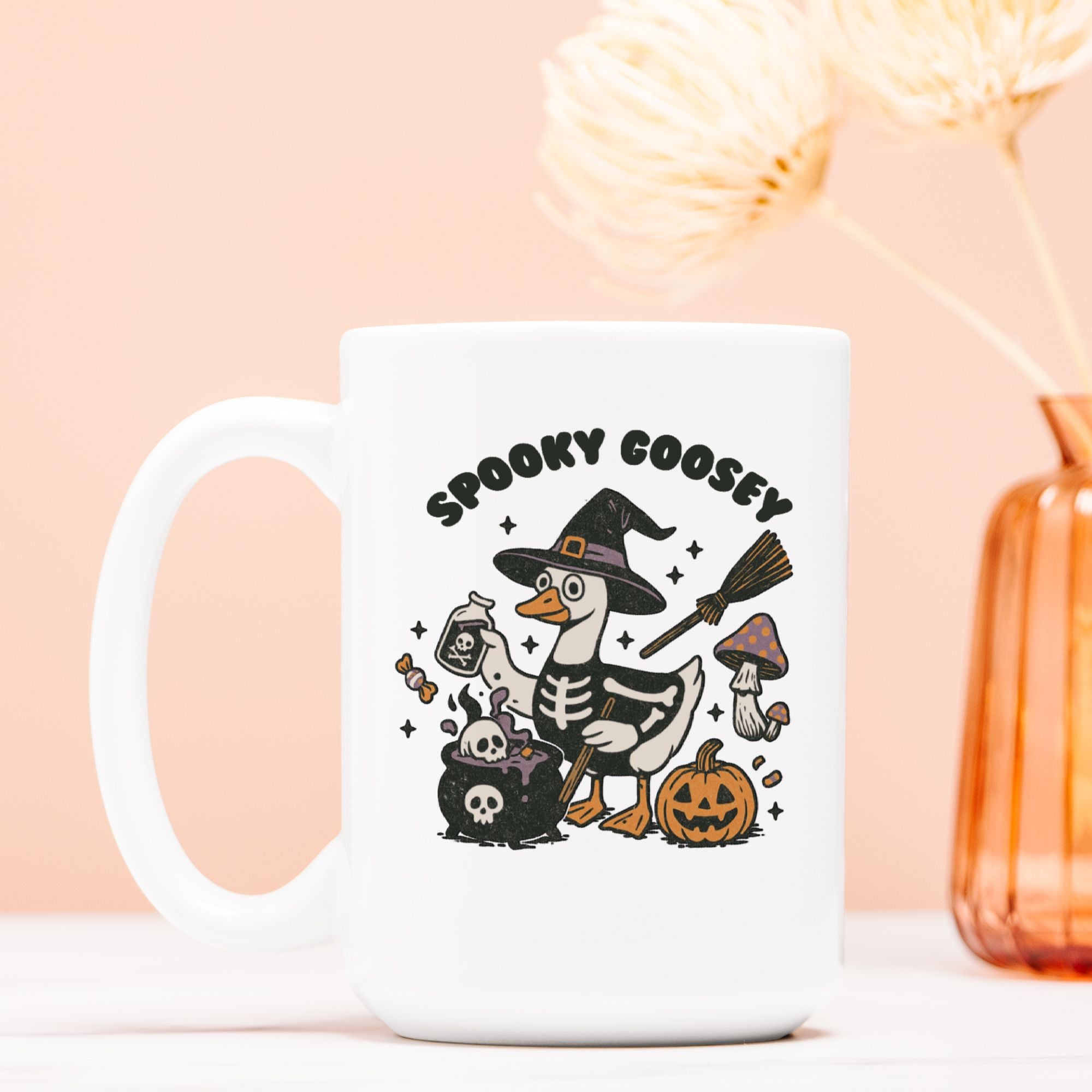 White mug with Halloween-themed design featuring a goose in a witch hat and skeleton costume, on a peach background.