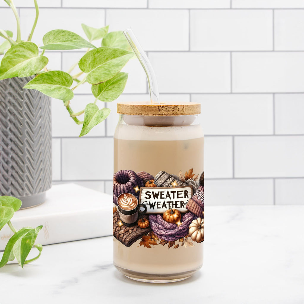 Candle jar with 'Sweater Weather' label on a white surface with a plant in the background