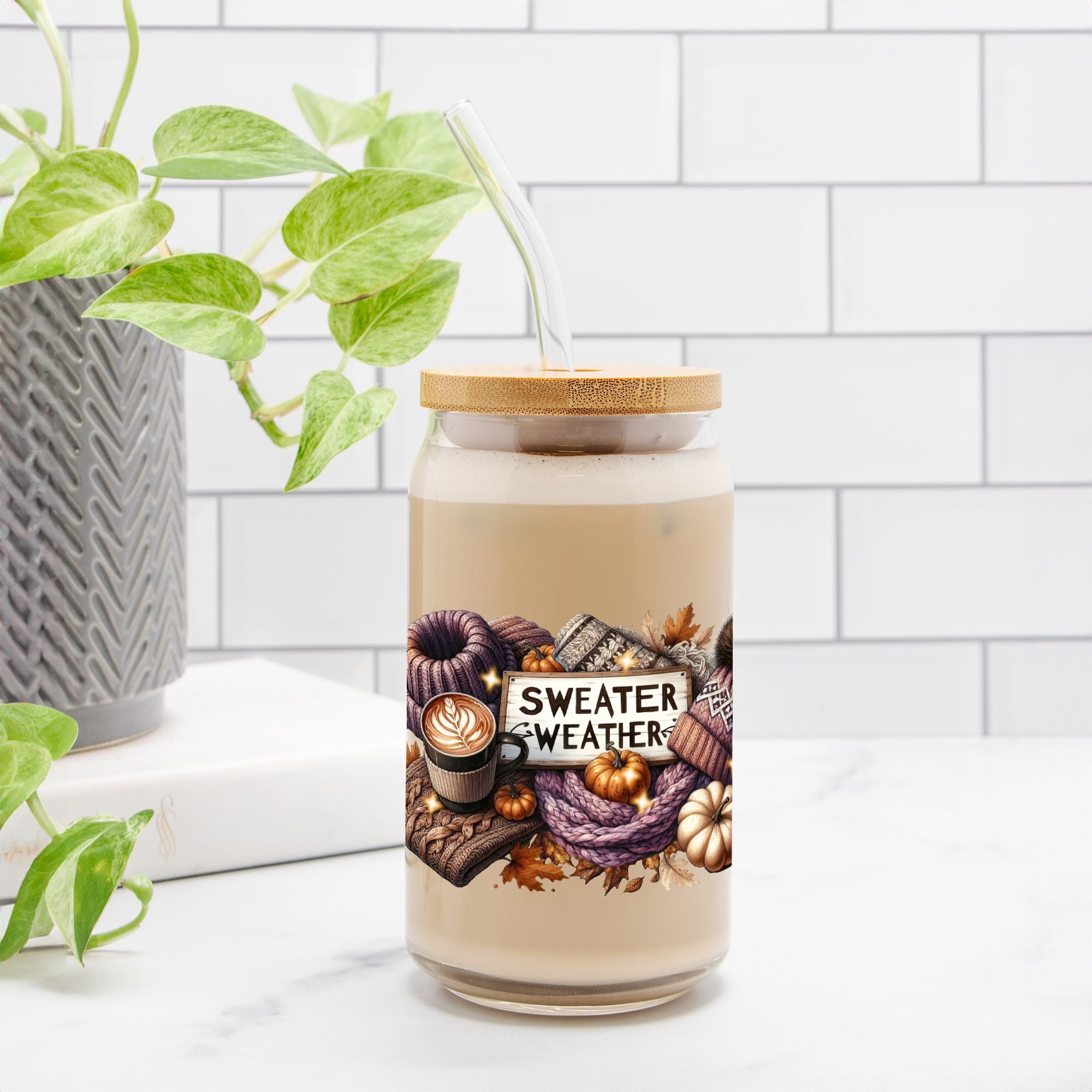 Candle jar with 'Sweater Weather' label on a white surface with a plant in the background