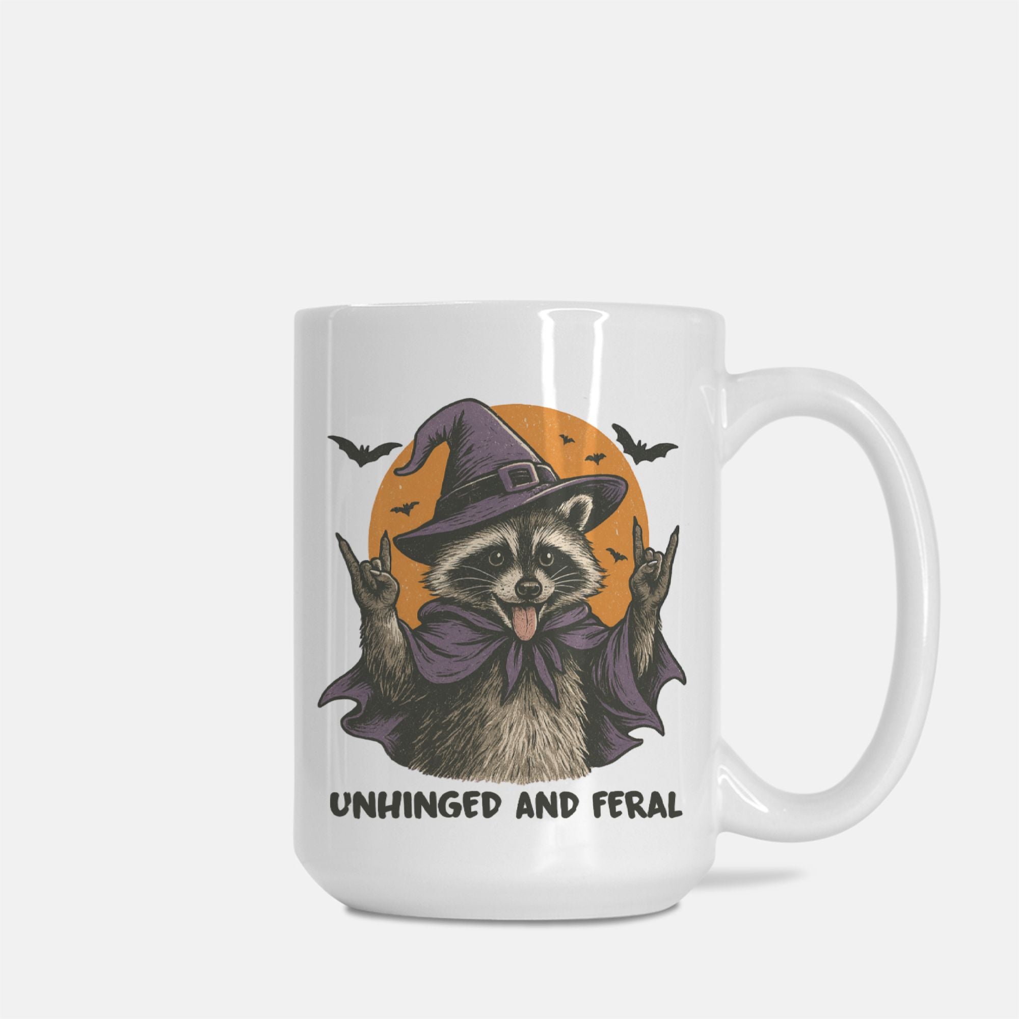 White mug with a raccoon in a witch hat design and text 'Unhinged and Feral' on a white background