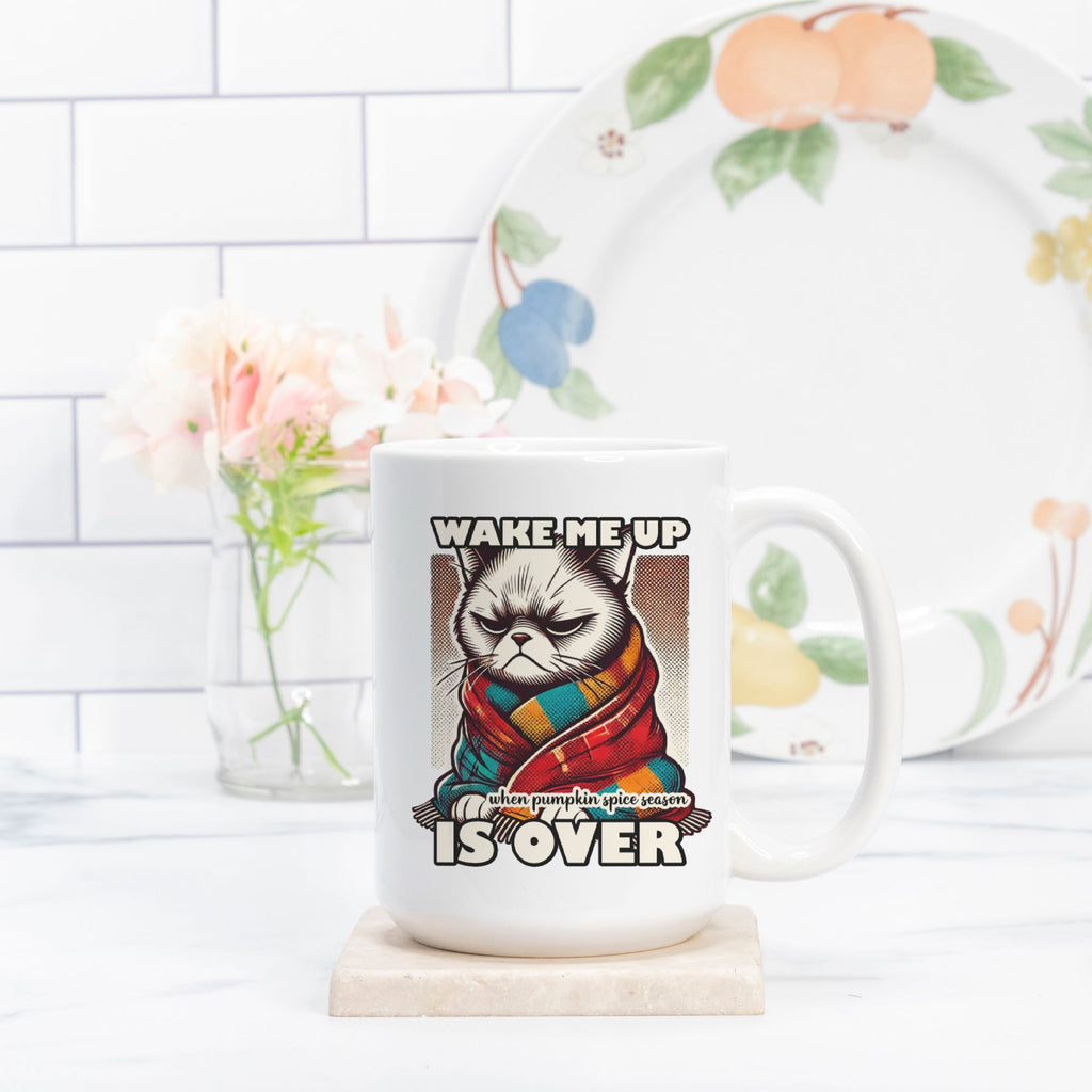 Mug with a cat design and text 'Wake me up when pumpkin spice season is over' on a kitchen counter.