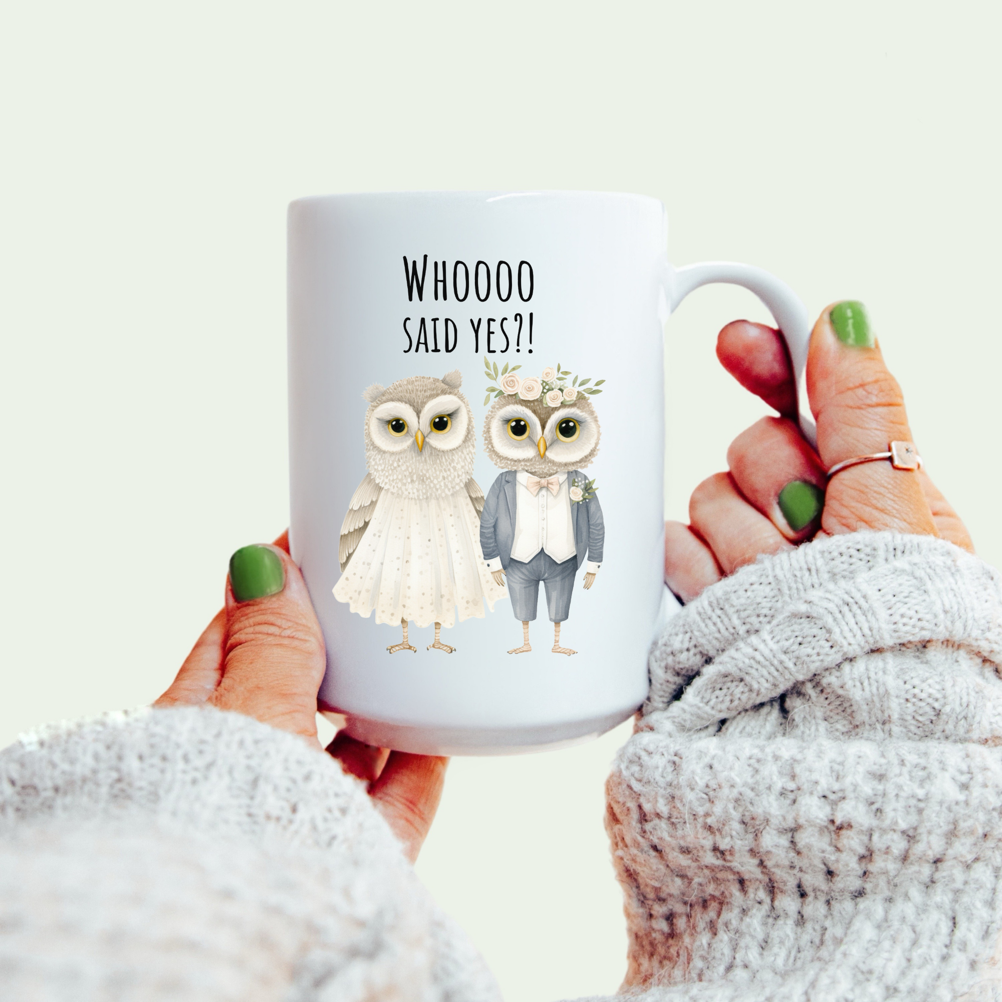 Mug with owl design and text held by a person wearing a white sweater.