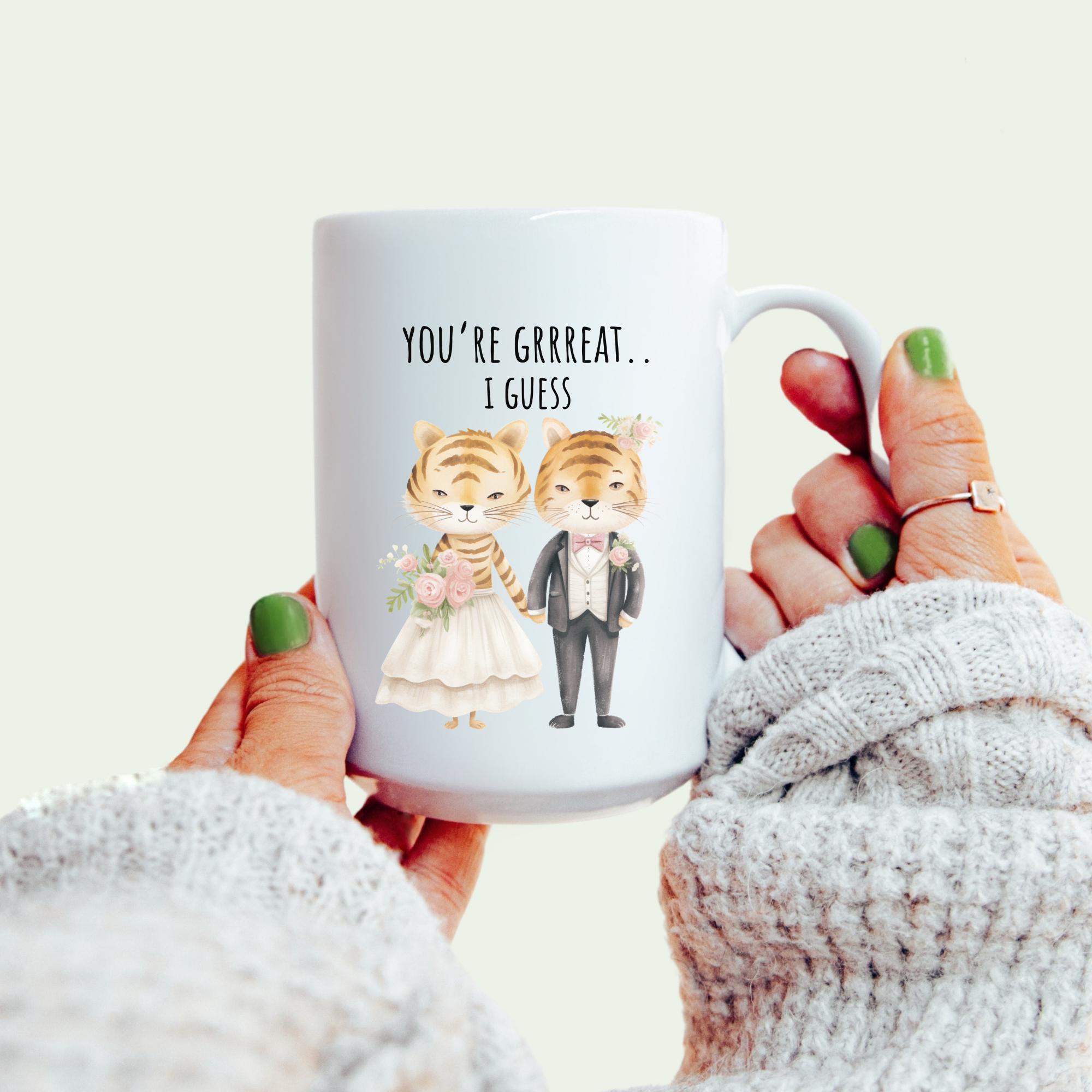 Mug with cartoon tigers and text held by a person wearing a white sweater.