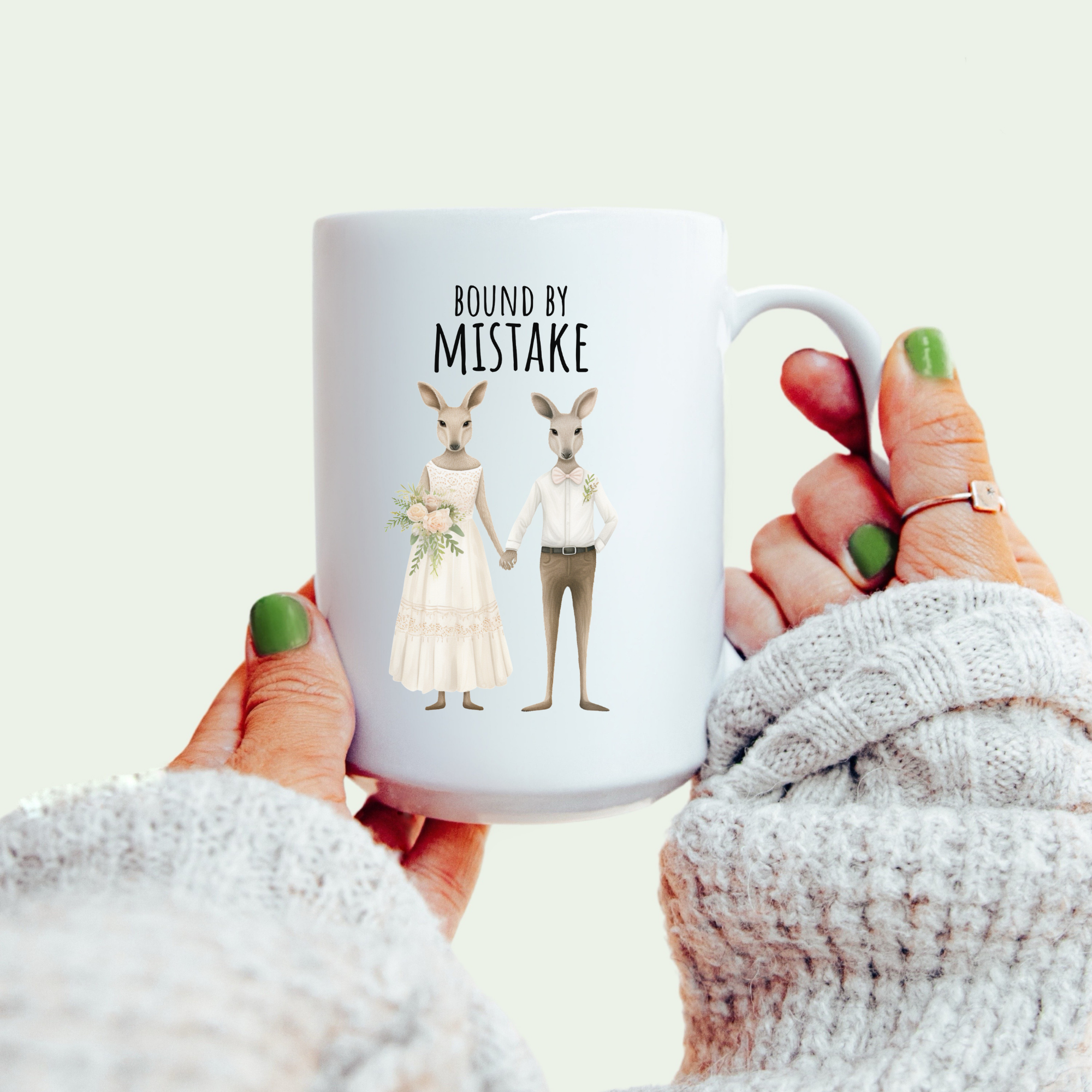 White mug with kangaroo couple design and 'Bound by Mistake' text held by a person.
