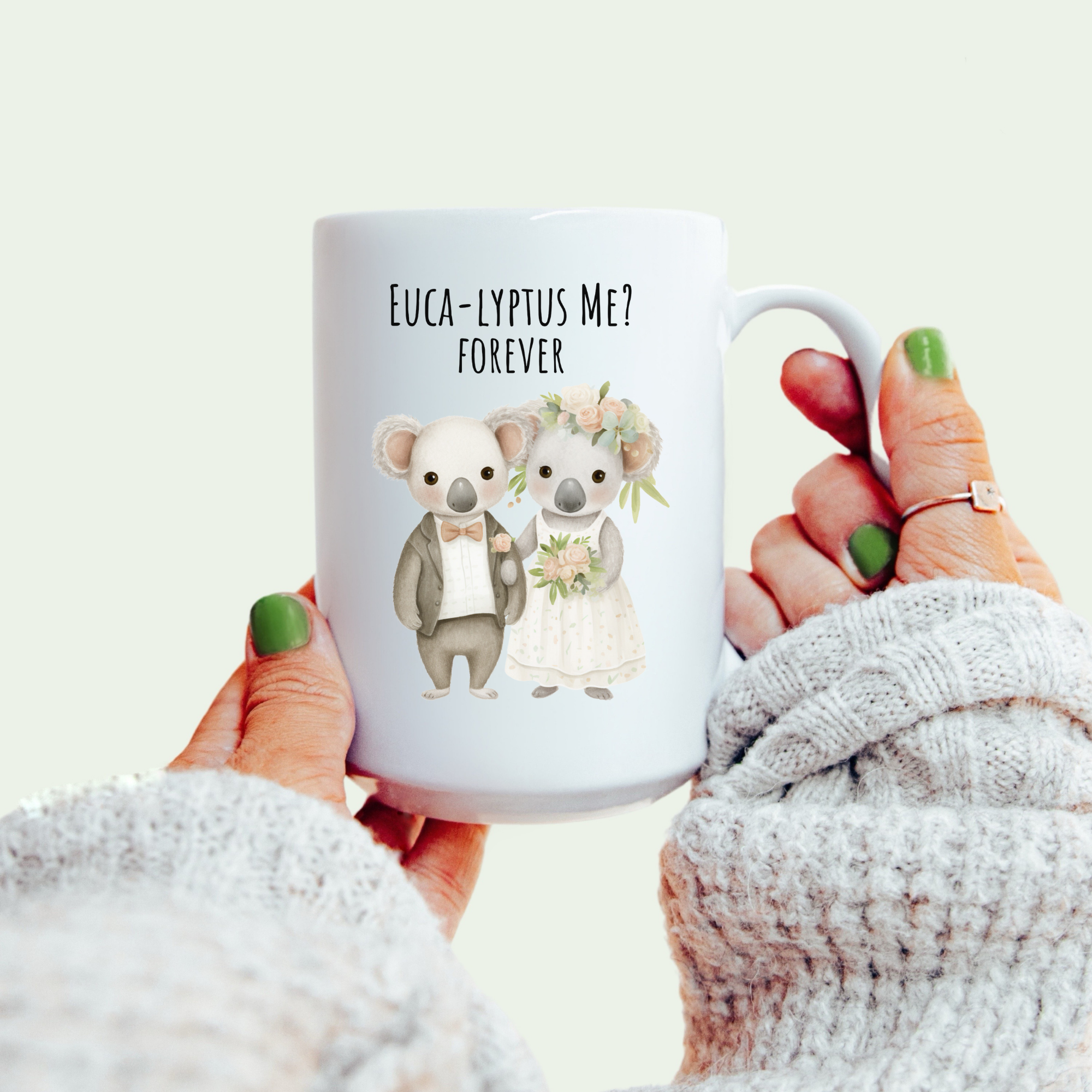 White mug with koala design and text held by a person wearing a white sweater.