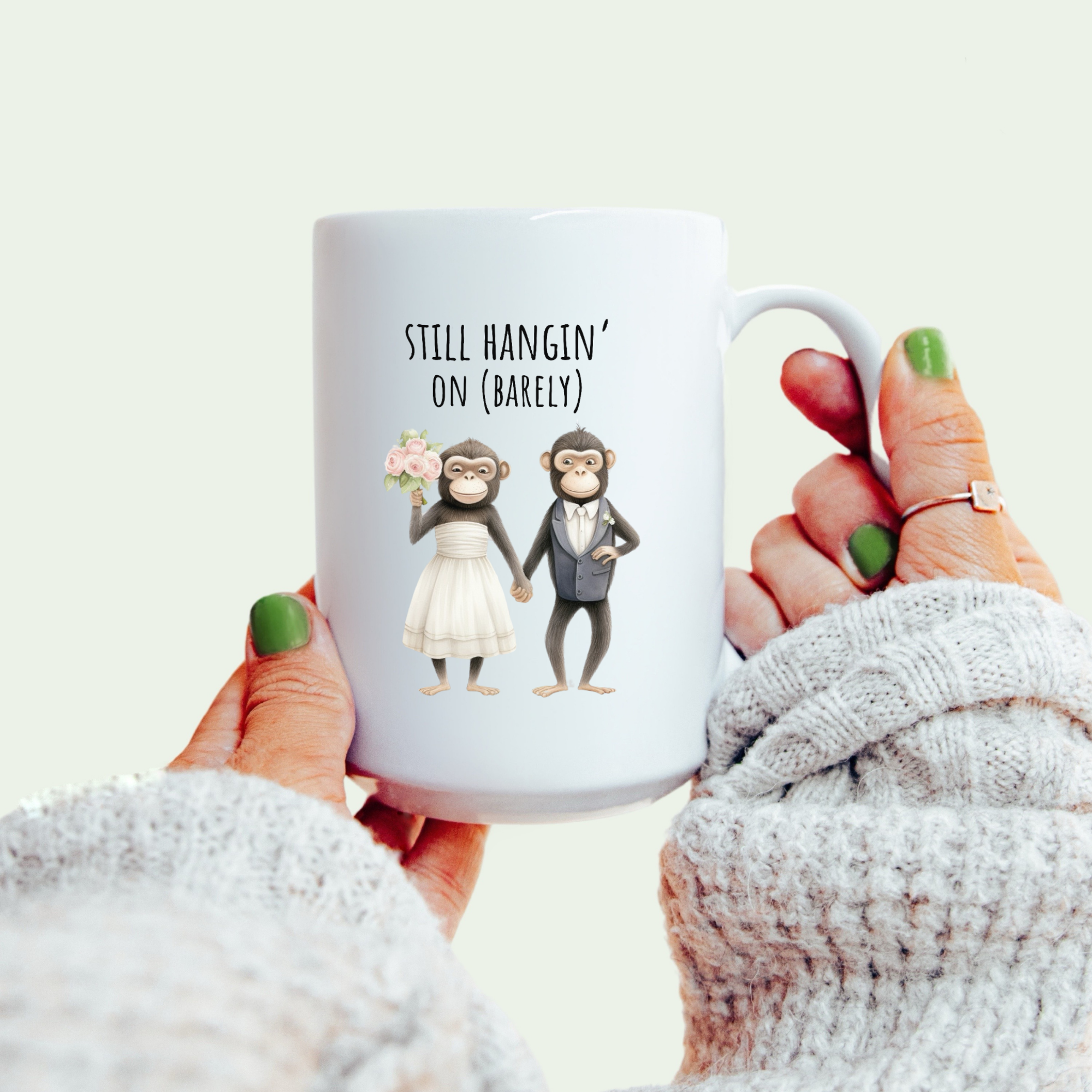 White mug with cartoon monkeys and text held by a person wearing a white sweater.