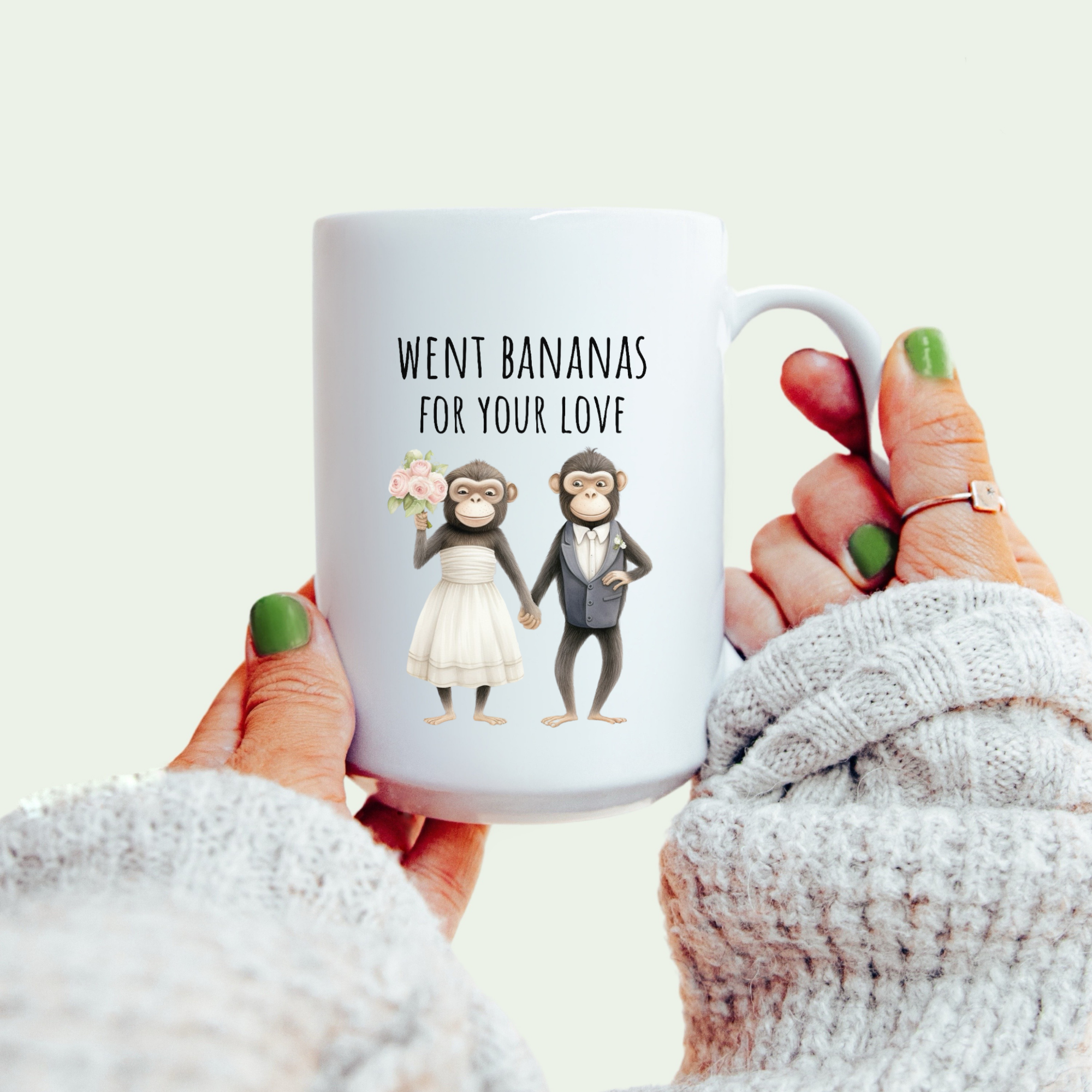 White mug with cartoon monkeys in wedding attire and text 'went bananas for your love' held by a person wearing a white sweater.