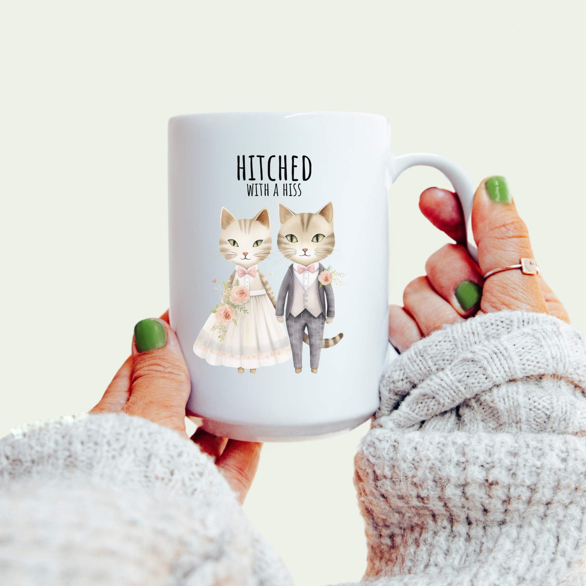 Mug with cartoon cats in wedding attire and 'Hitched with a Hess' text, held by a person.
