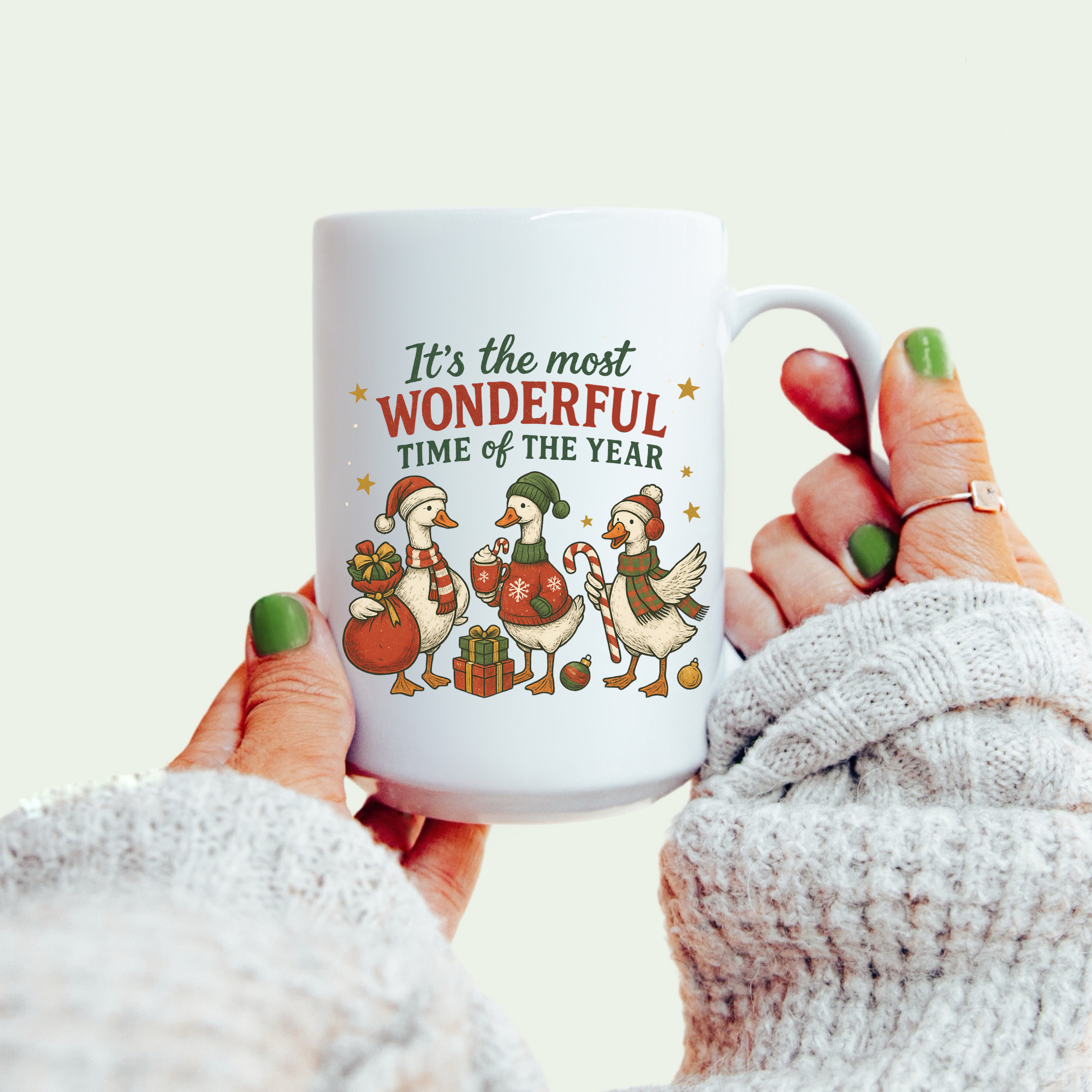 White mug with Christmas design and text held by a person wearing a white sweater.